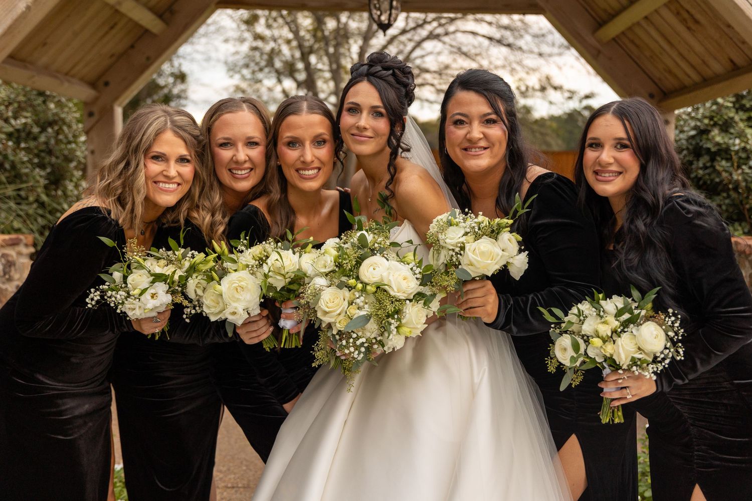 Wedding party poses with white floral bouquets outdoors.