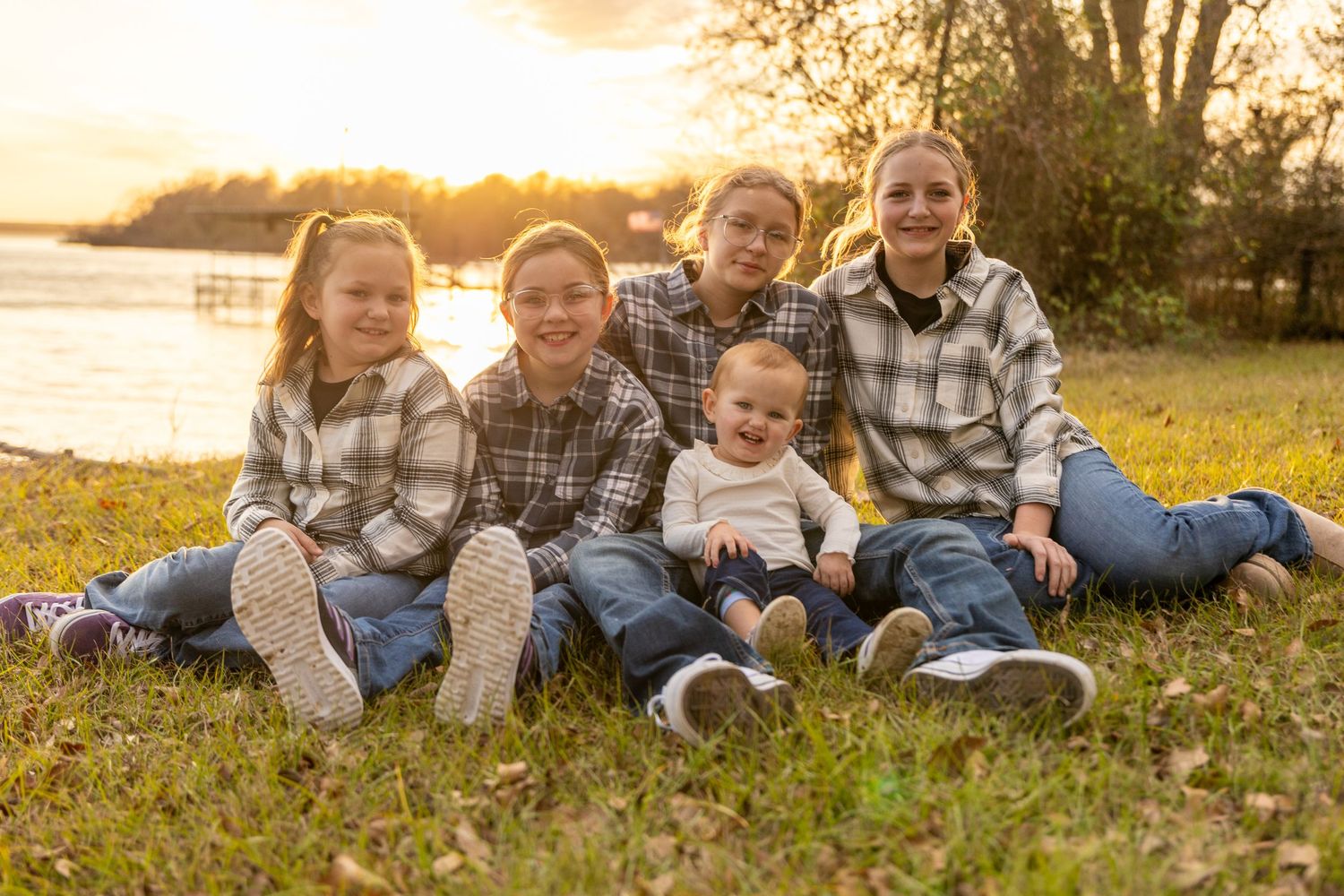 Family sitting together on autumn grass during golden hour by the water.