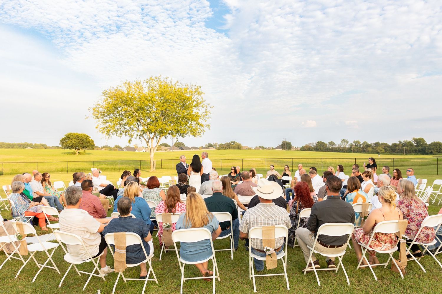 Wedding guests seated in white chairs for an outdoor ceremony with a scenic countryside backdrop.