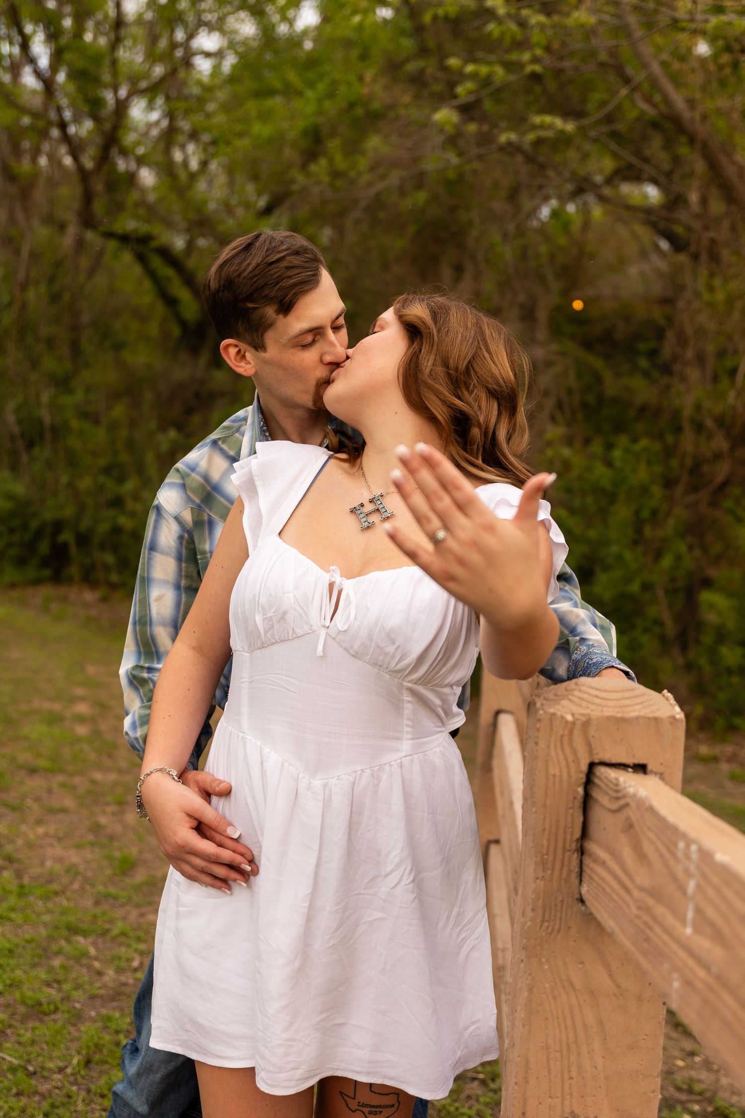 A tender moment shared between a couple near a wooden fence in a natural setting.