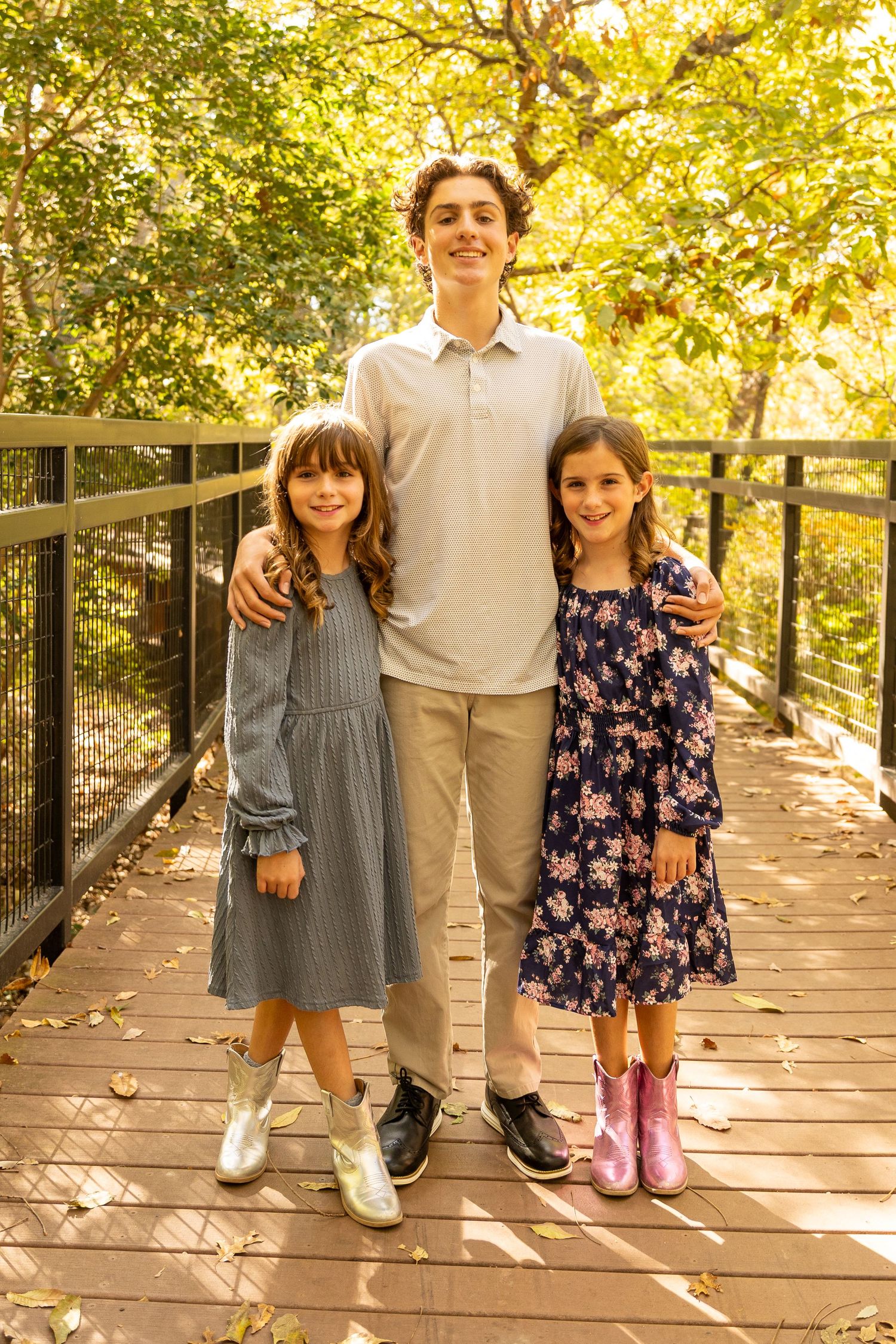 Children lined up on wooden boardwalk during fall family photoshoot with golden lighting.