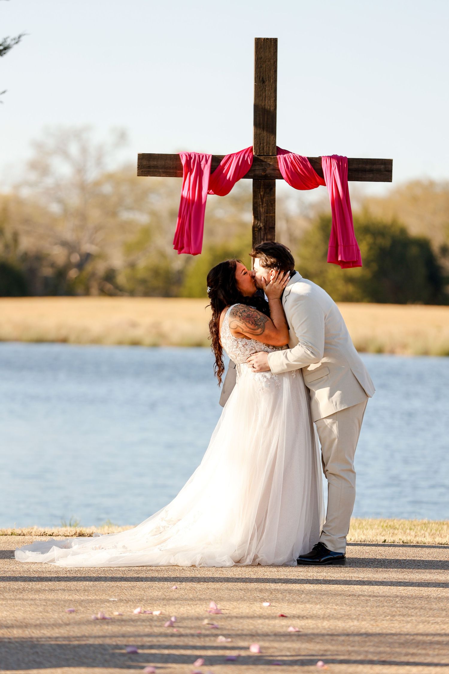 Wedding ceremony setup by a lake with wooden cross draped in red fabric.