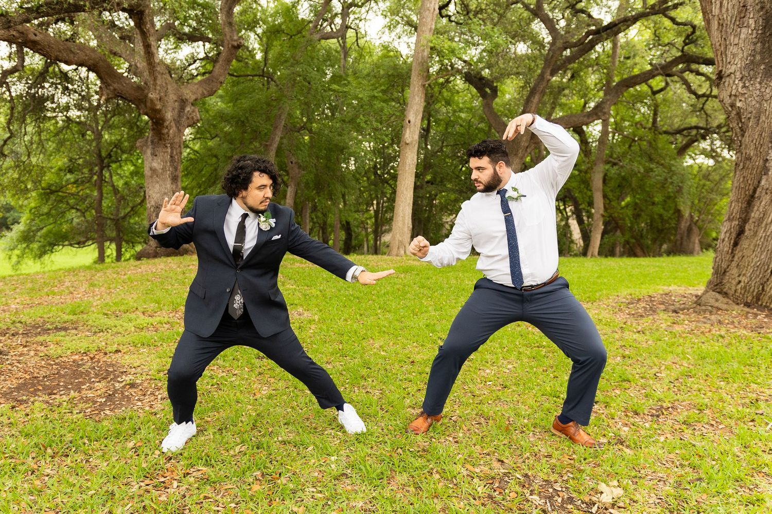 Wedding party members strike playful jumping poses on grassy lawn.