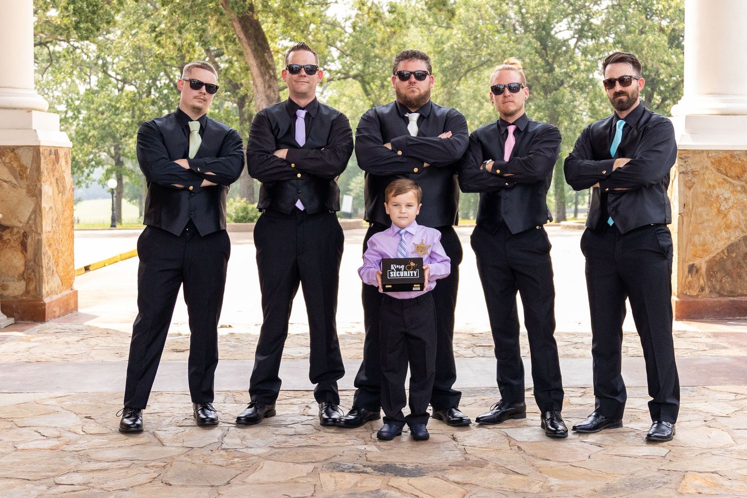 Groomsmen in black suits and sunglasses pose in a fun lineup outdoors.