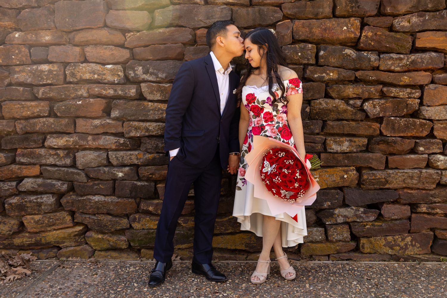 A couple shares an intimate moment against a rustic stone wall background.