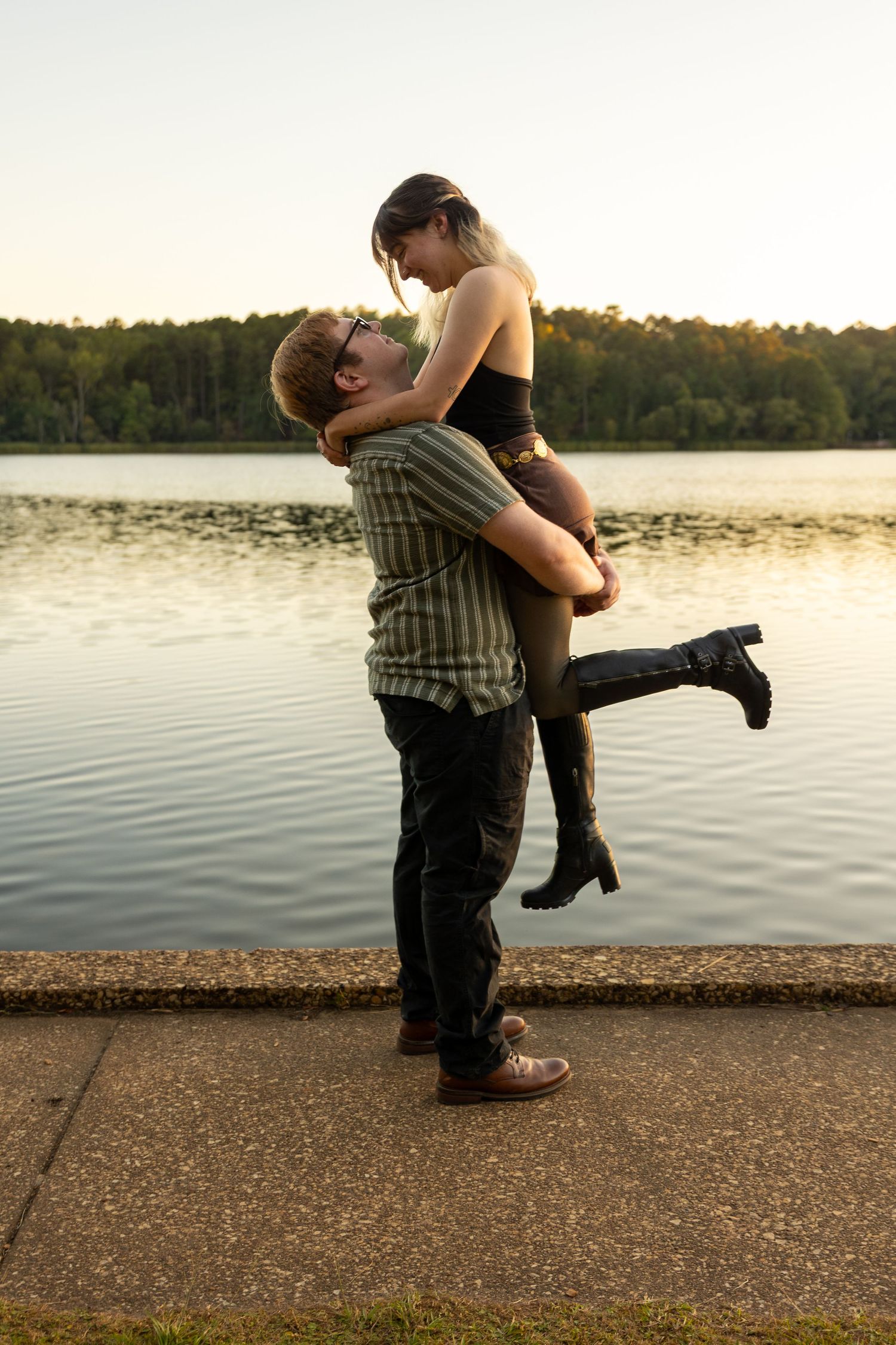 Romantic couple poses by the lakeside during sunset in a playful lifting sequence.