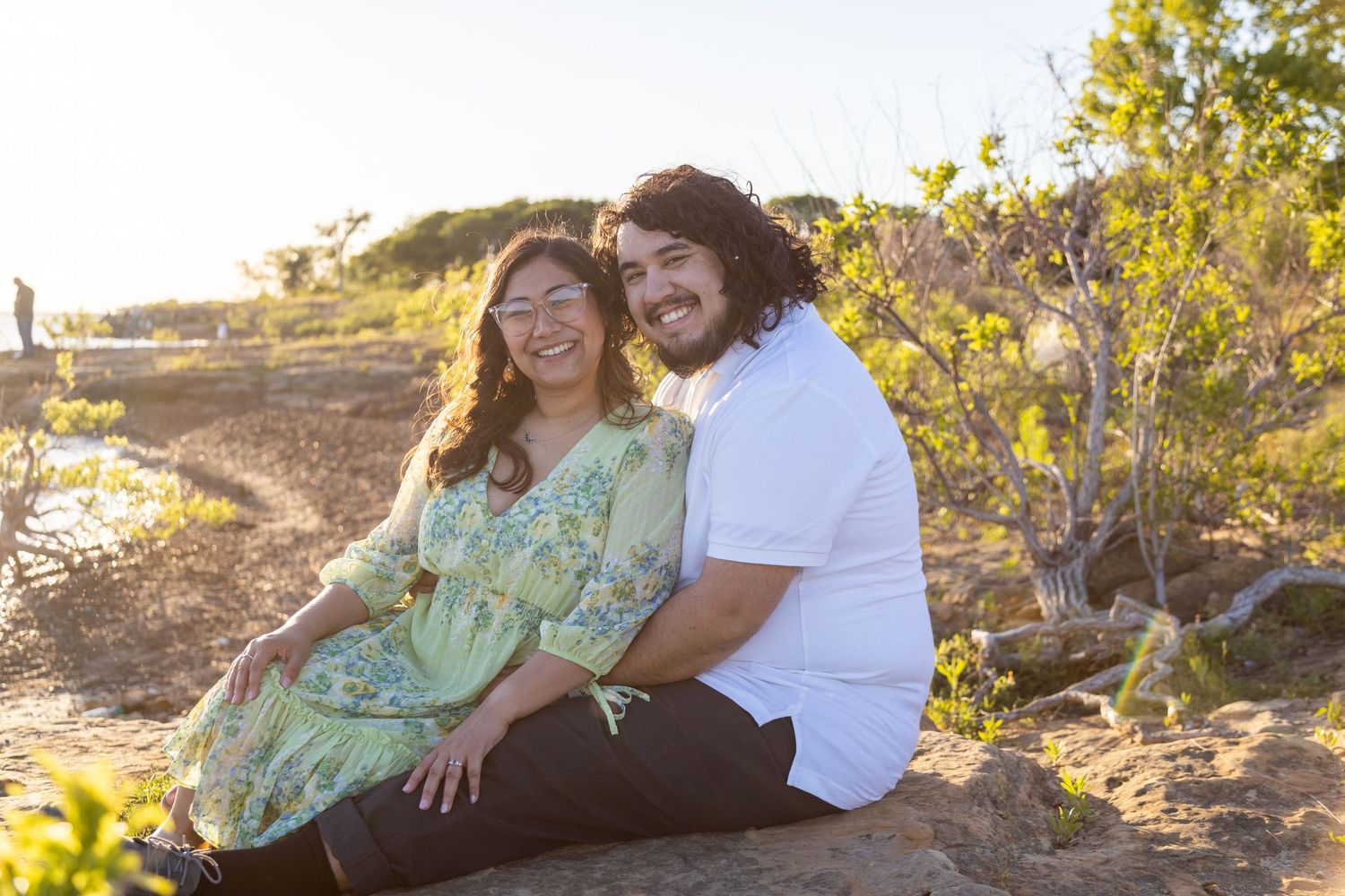 Couple embraces in golden sunlight against natural outdoor backdrop during romantic photoshoot.