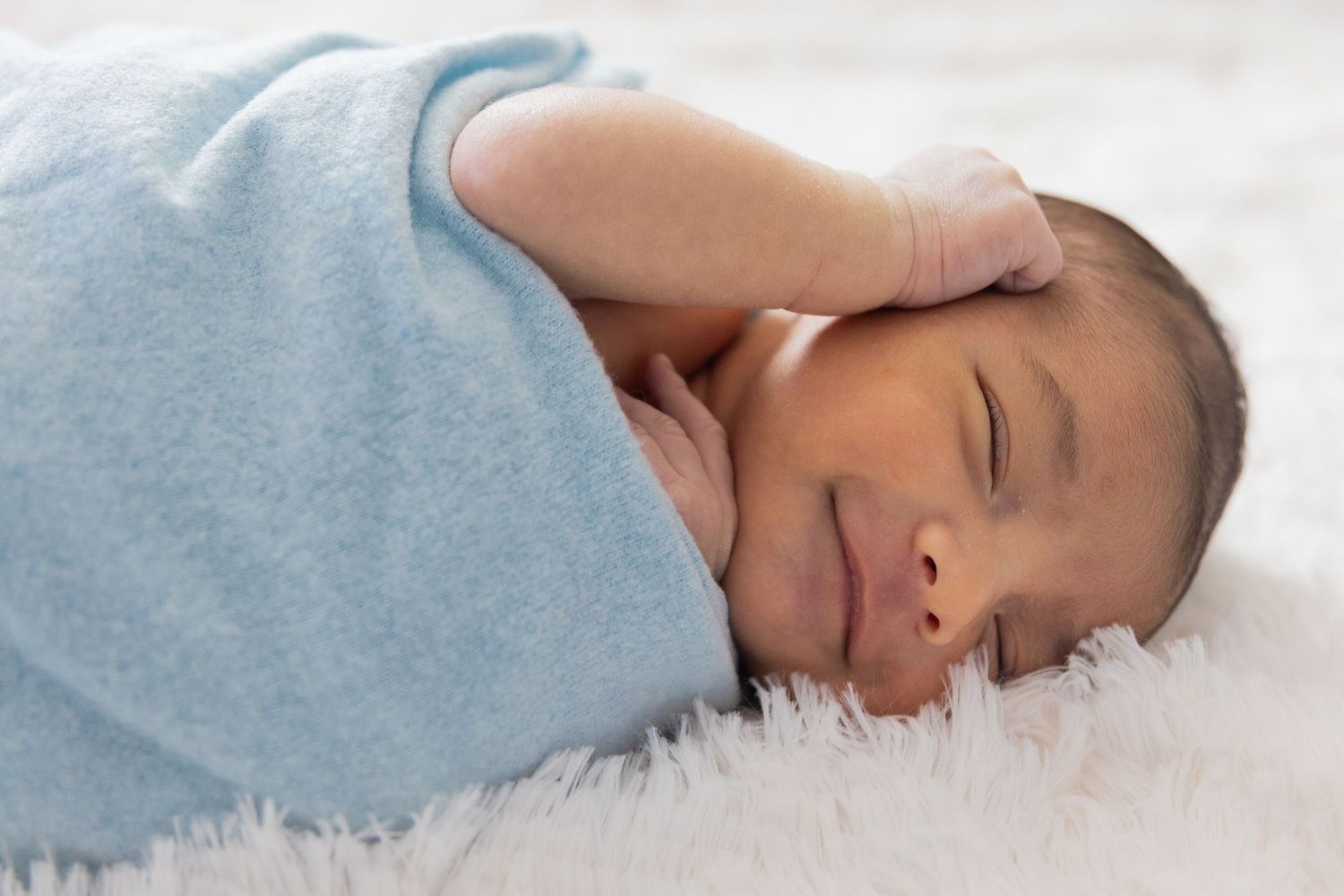 Sleeping newborn swaddled in light blue blanket on white background.