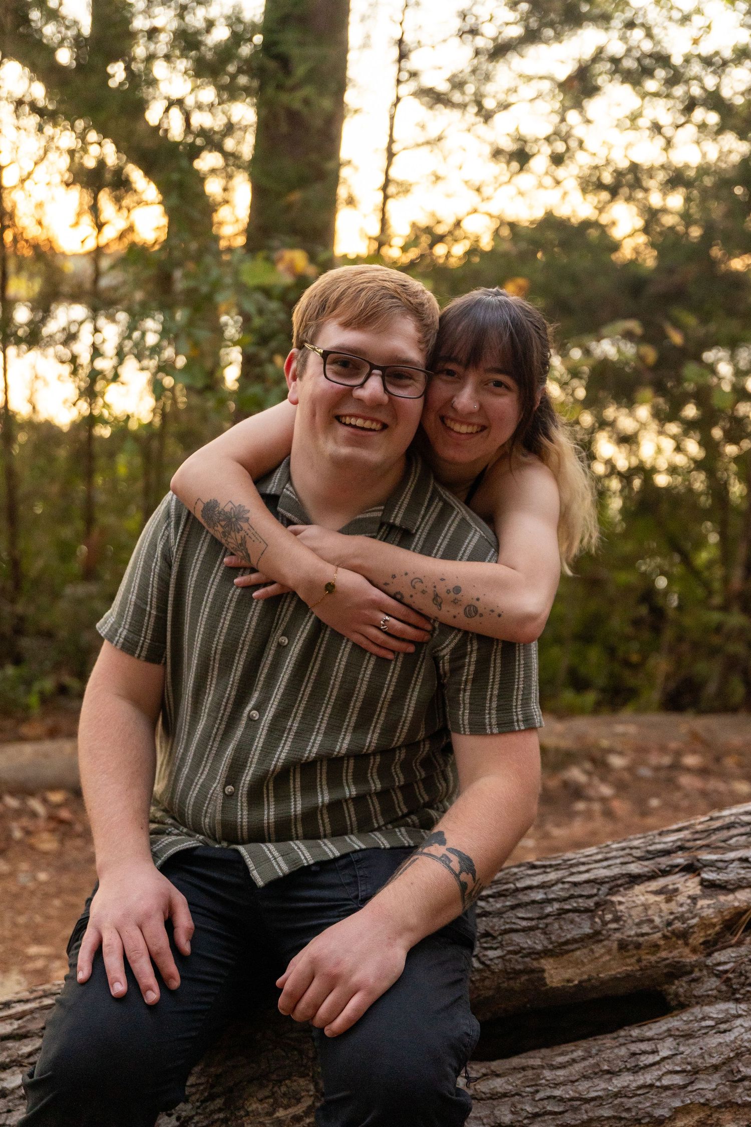 Couple sitting together on a fallen log in a forest during golden hour.