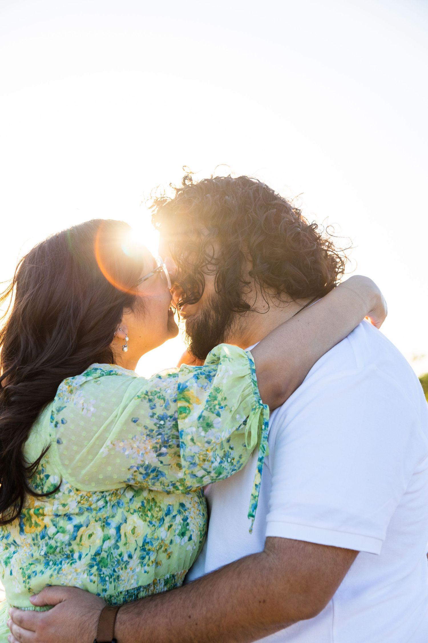 Close-up of couple in mint green and white clothing during intimate sunset moment.