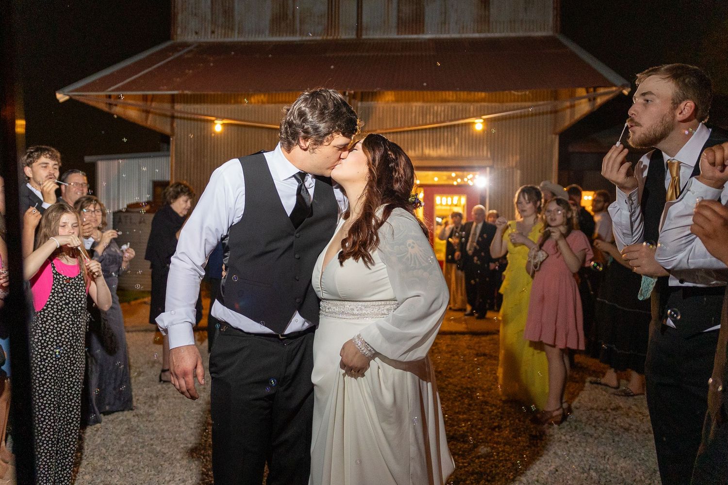 Wedding guests dance and celebrate during an evening reception in a warmly lit indoor venue.