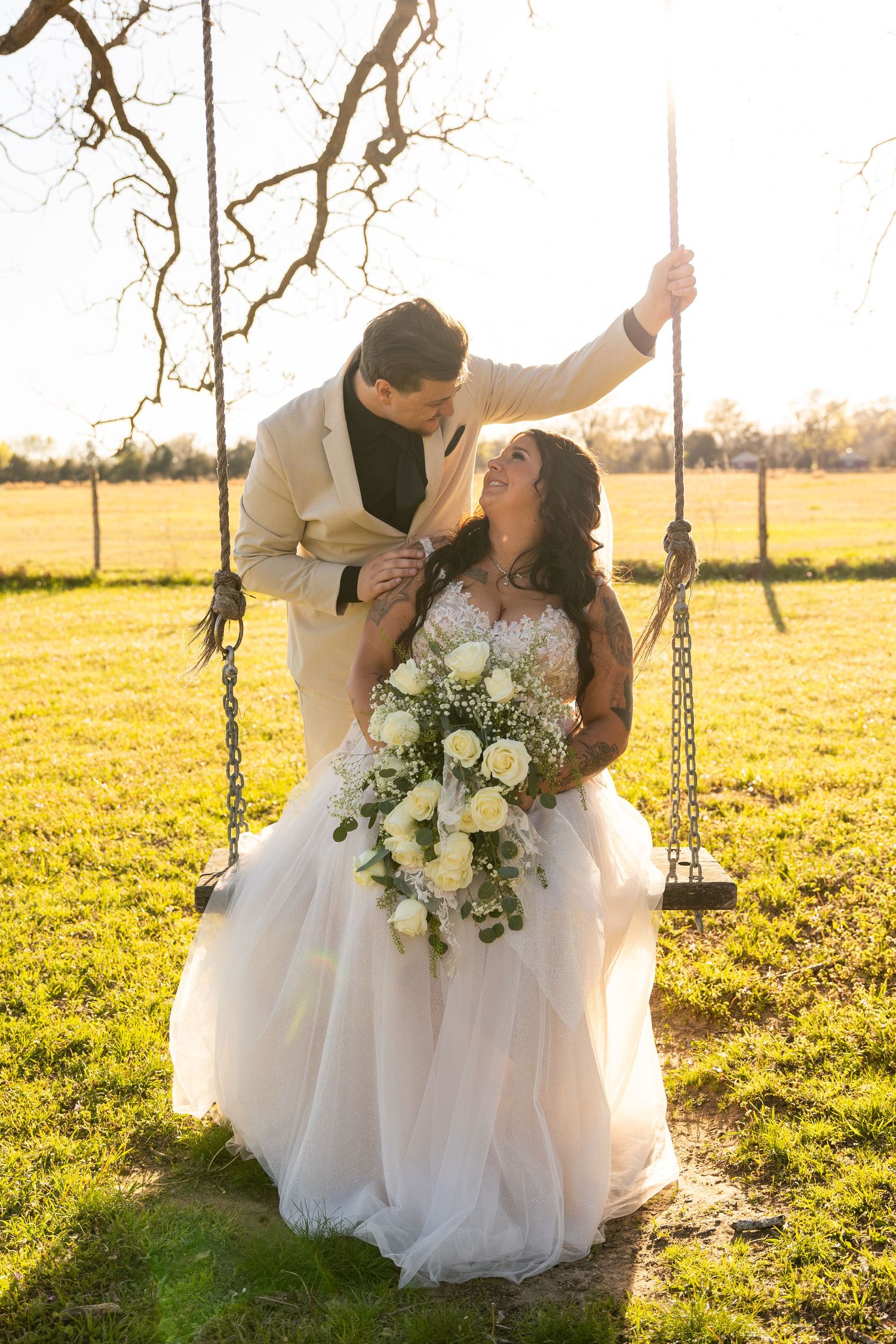 Romantic swing photos in a sunlit field with white floral bouquet.