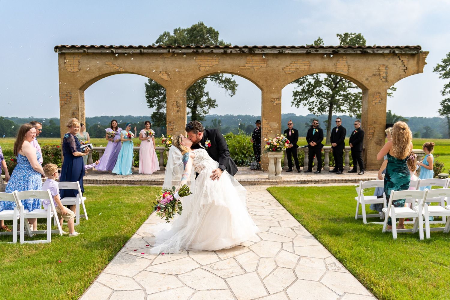 An outdoor wedding venue with white chairs set up under stone archways overlooking a scenic landscape.