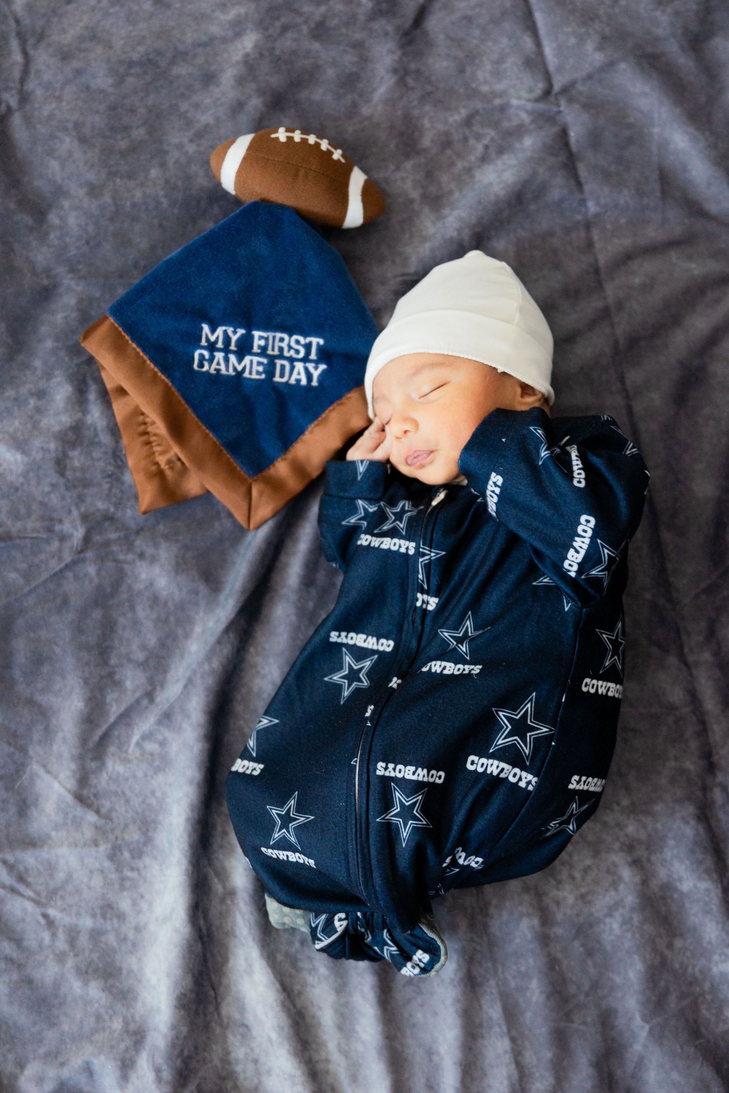 Dallas Cowboys themed baby items including onesie and football on gray background.