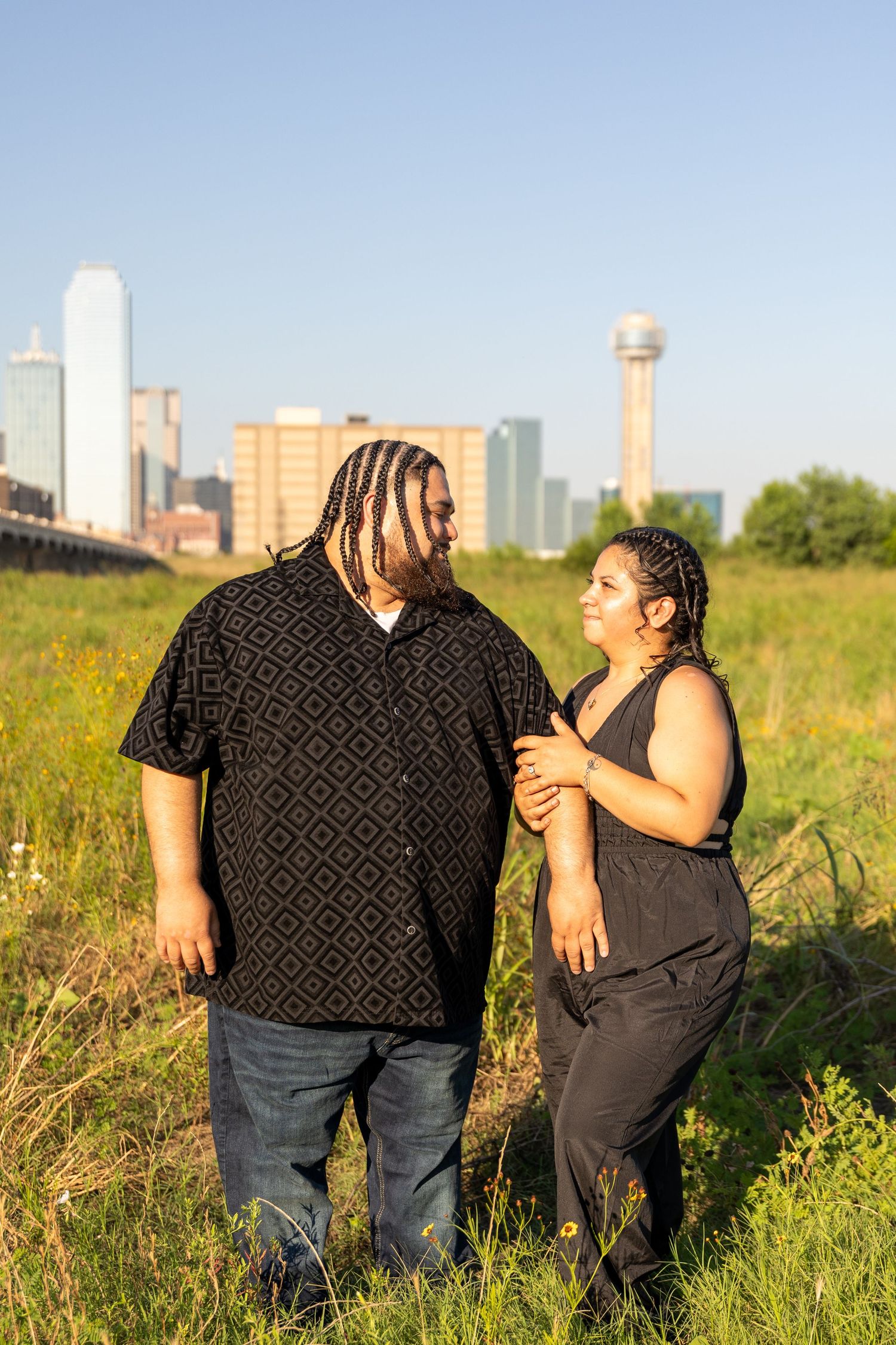 Couple sharing intimate moments in wildflower field with urban skyline in background.