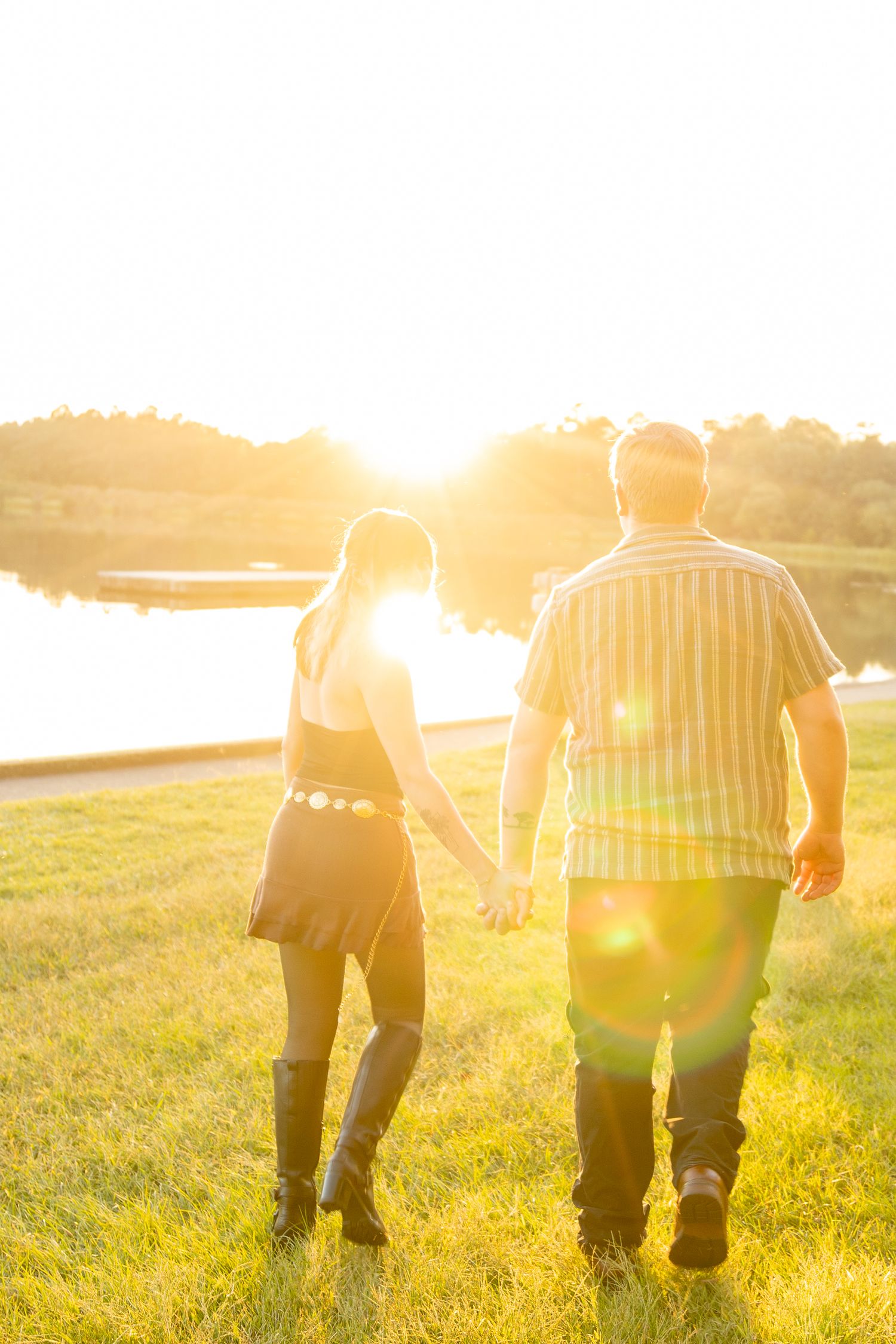 Silhouettes of a couple walking hand in hand during golden hour with lens flare.