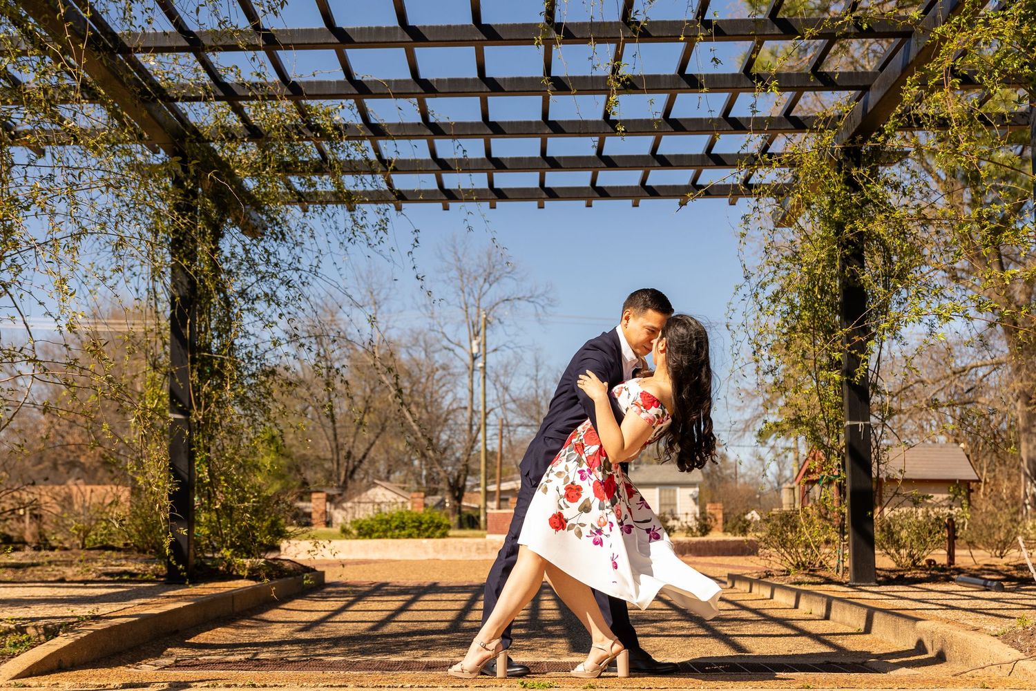 A romantic dip pose under a wooden pergola in an outdoor garden setting.