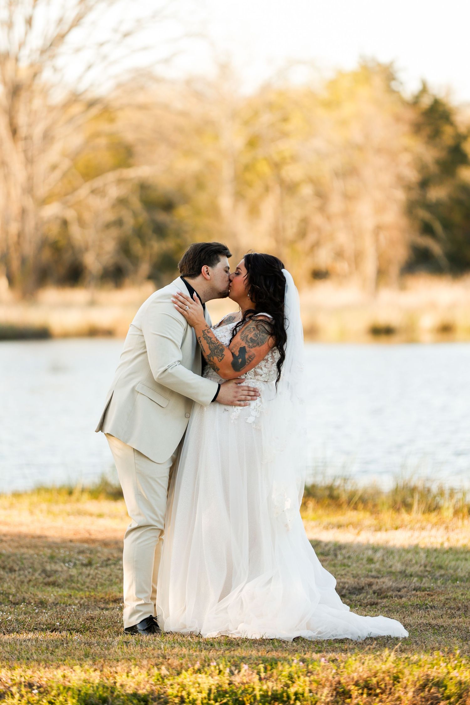 Romantic wedding portraits by a lake during golden hour with couple in white and beige attire.