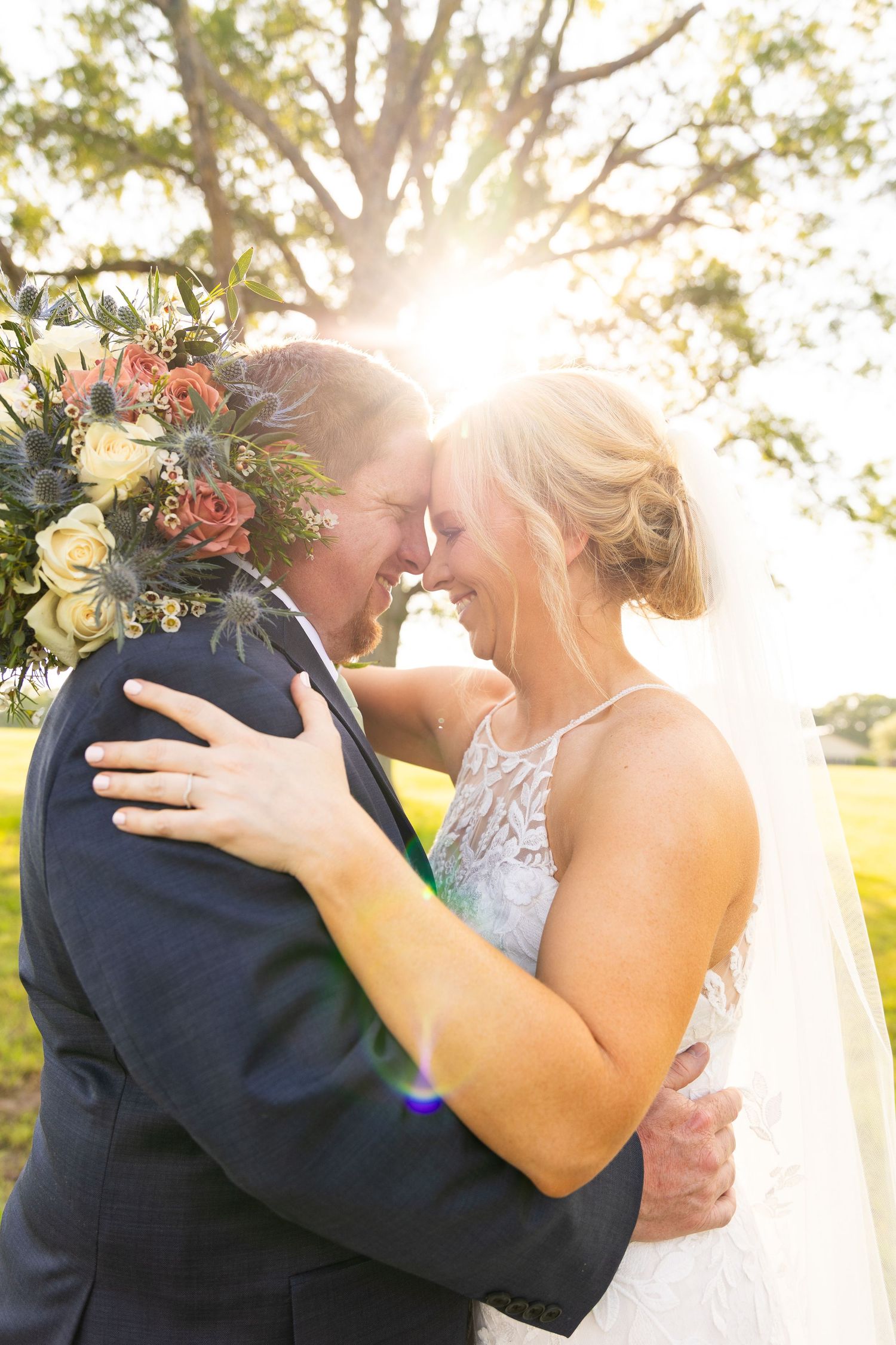 Newlyweds share intimate moment in golden sunlight with bride's veil flowing in breeze.