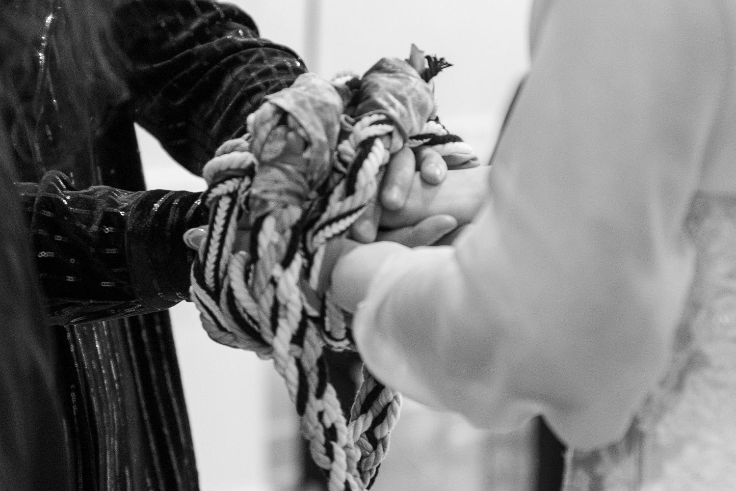 Black and white photo of hands joined together with braided rope in a handfasting wedding ceremony ritual.