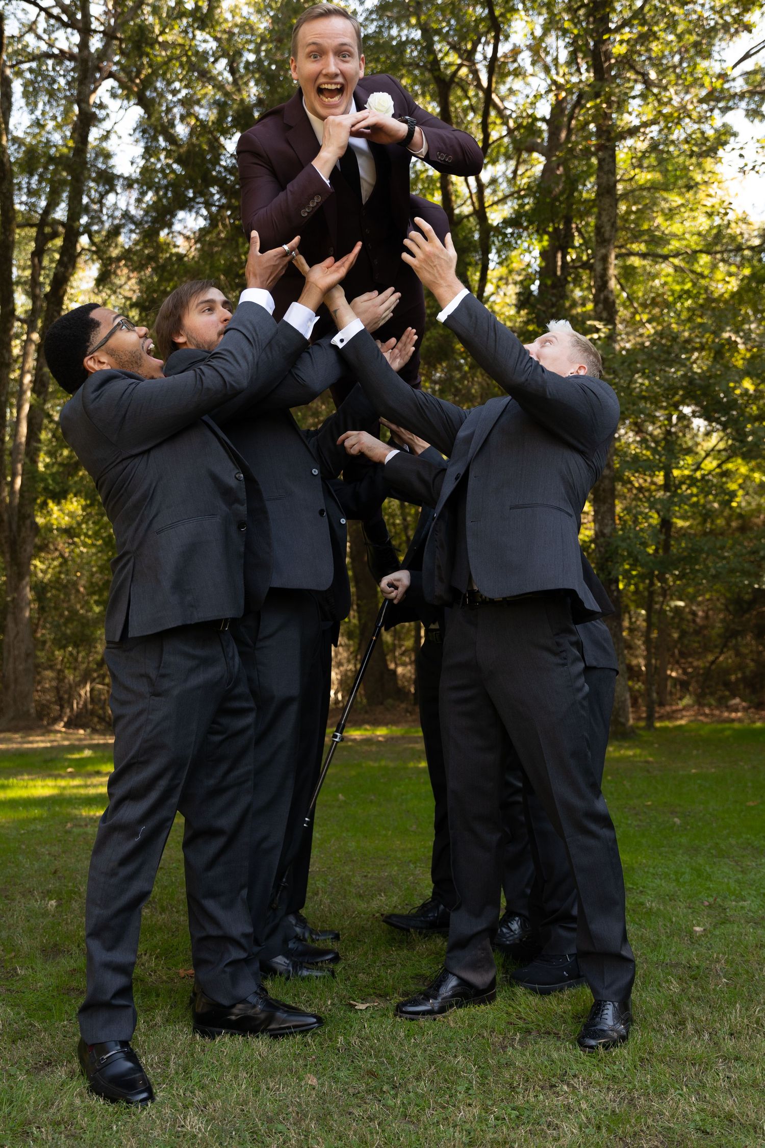 Groomsmen in black suits having fun with playful jumping poses outdoors.