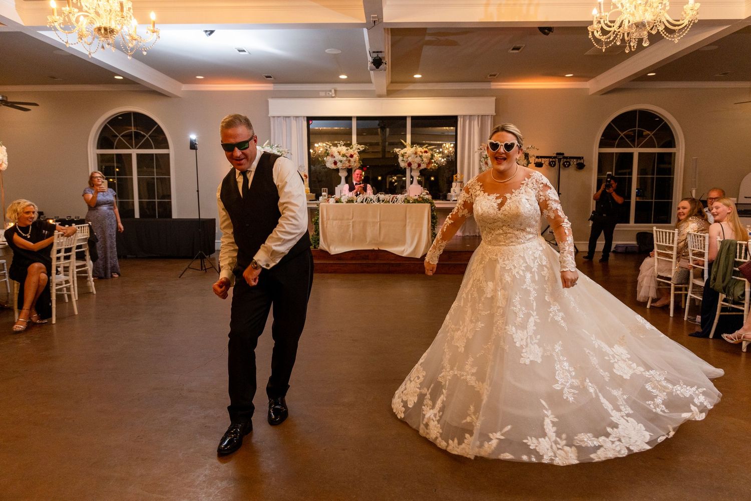 Wedding reception dance floor with guests dancing and celebrating under elegant chandeliers.