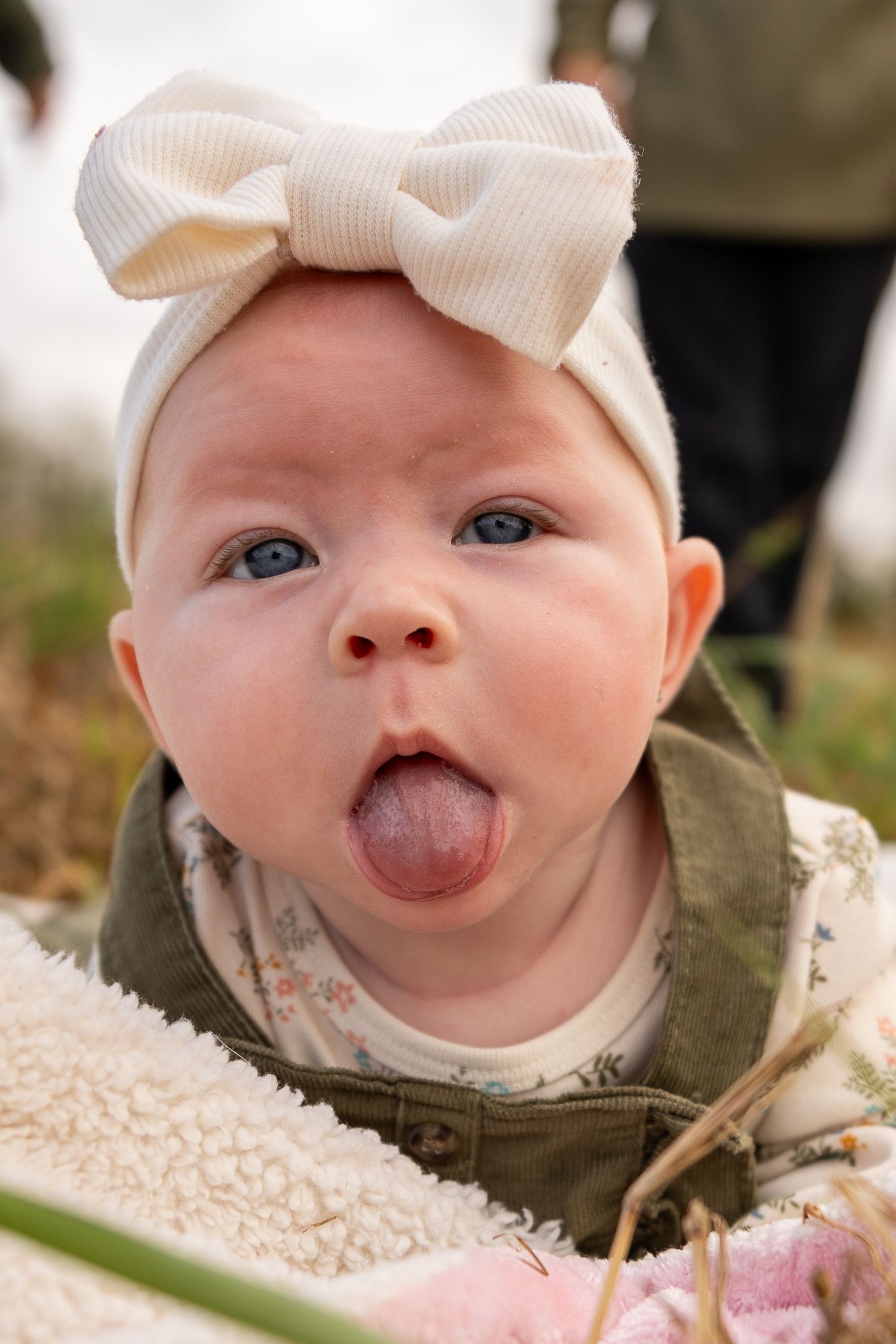 Baby wearing white bow headband making playful expressions at camera.