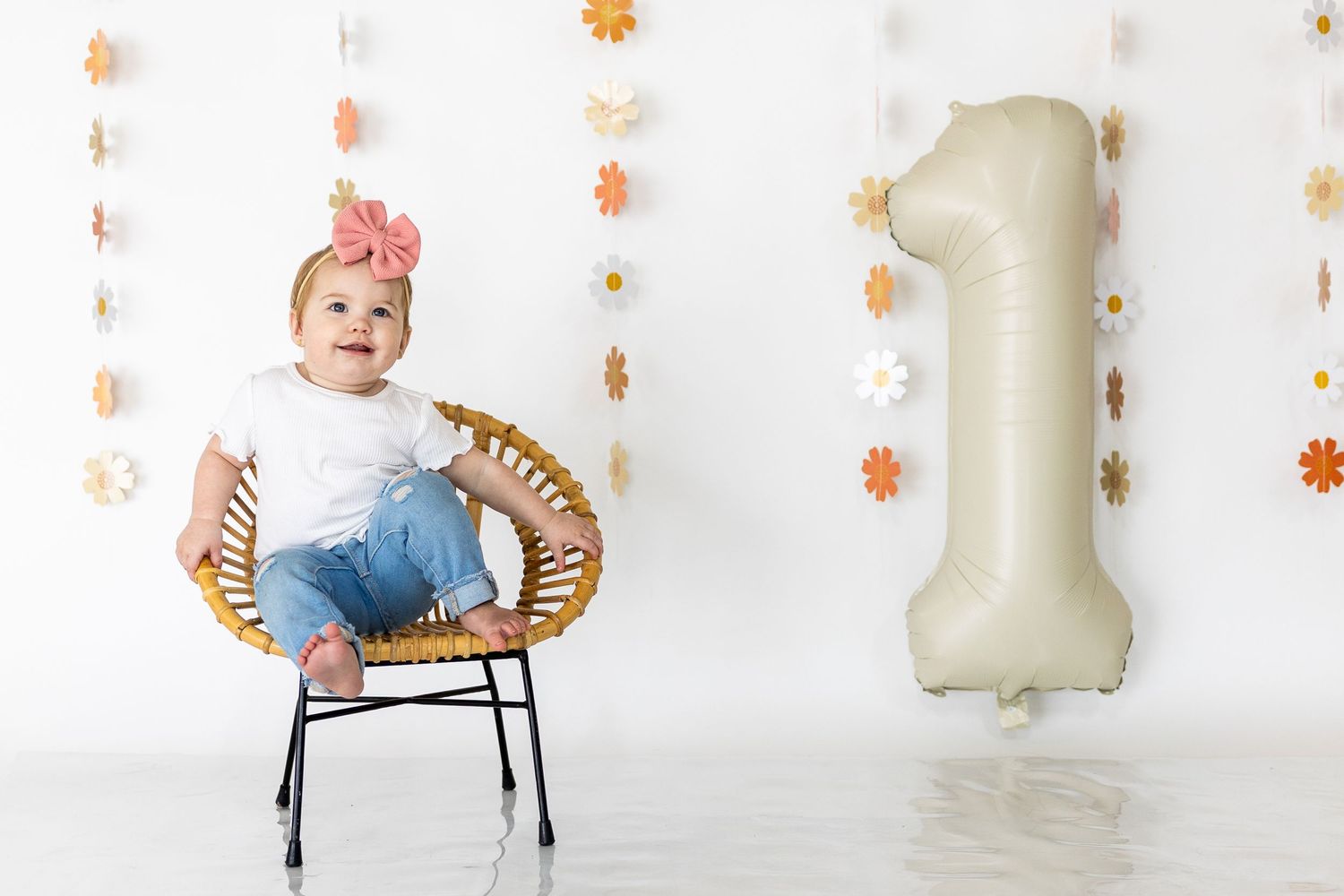 White backdrop with delicate orange flower decorations and number one balloon.