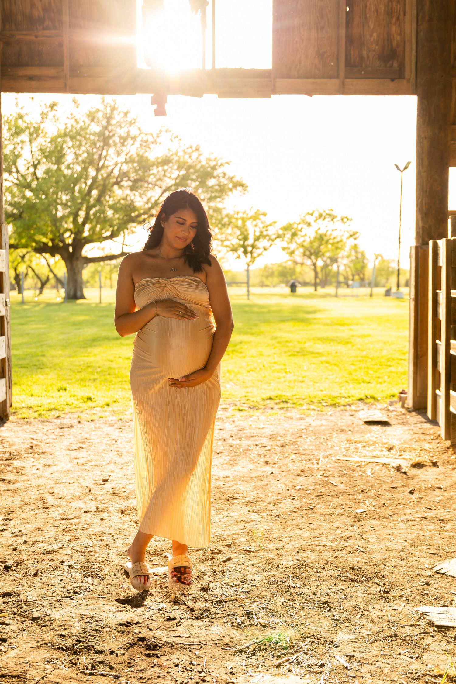 Maternity photoshoot in white dress during golden hour under wooden structure.