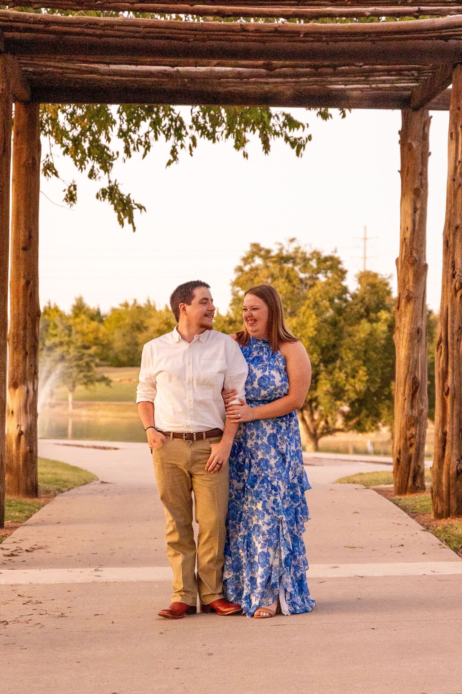 Couple sharing a romantic moment under a rustic wooden pergola at sunset.