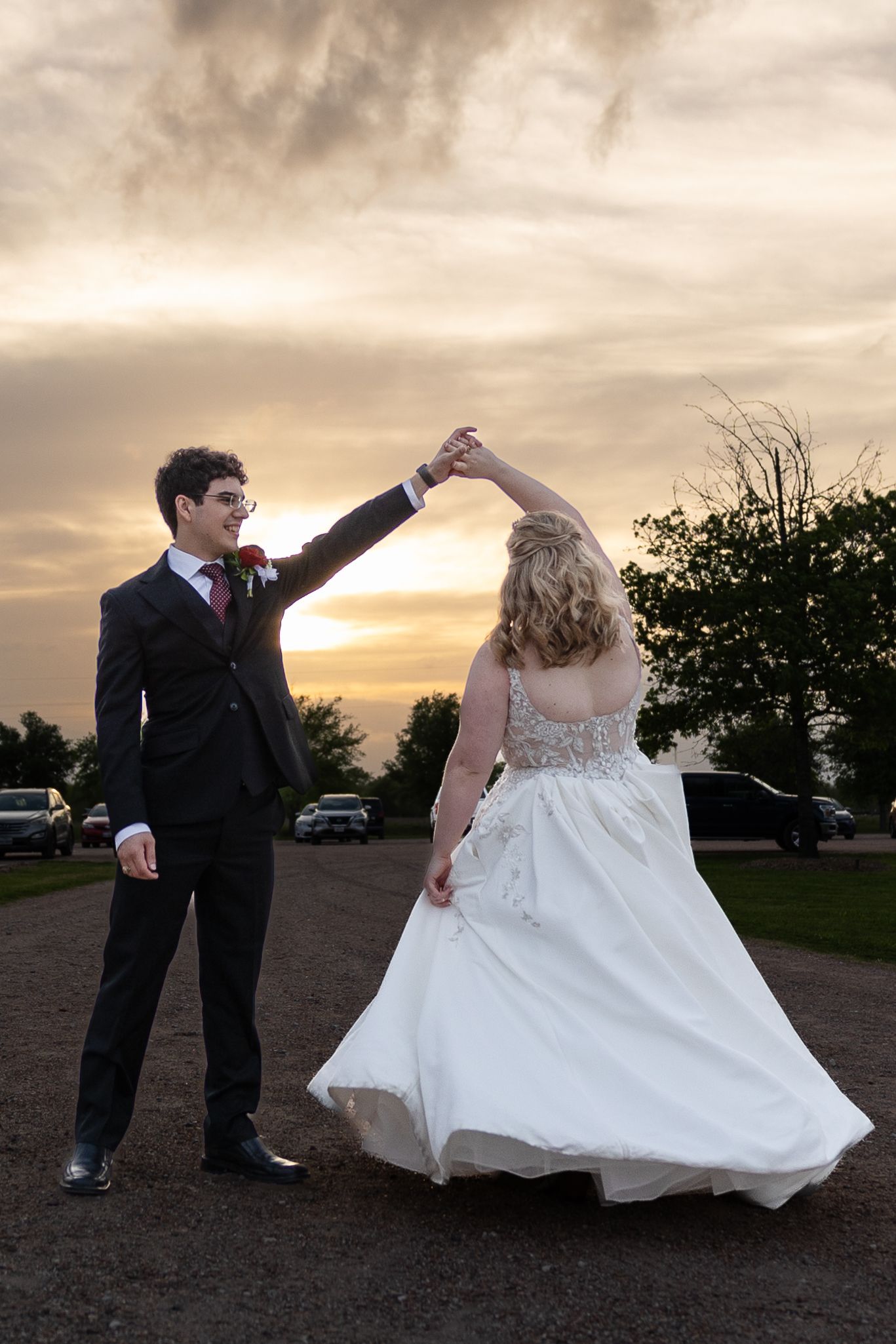Wedding couple dancing and twirling at sunset in an open field.