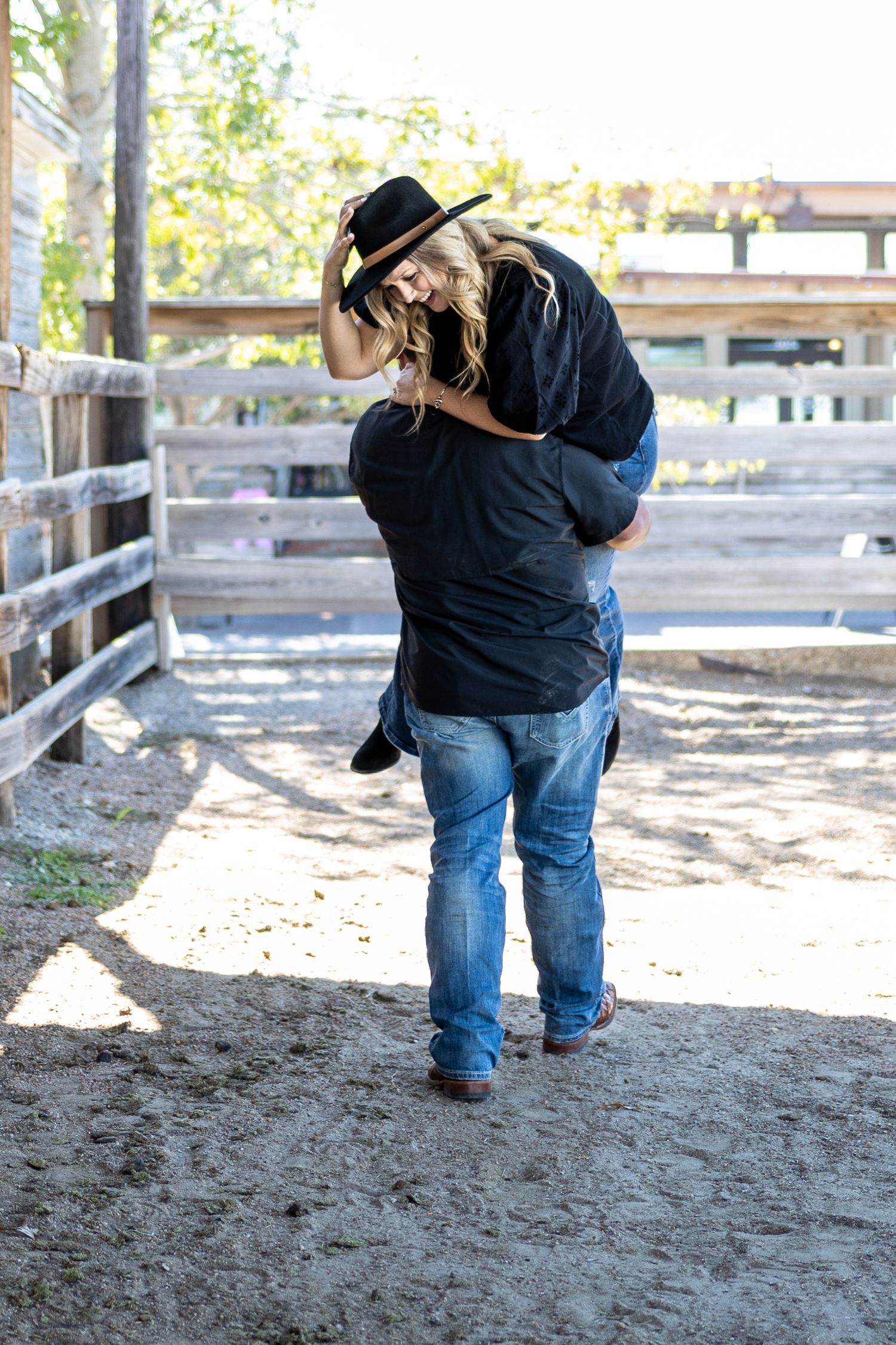 A playful couple poses in a rustic outdoor setting with wooden fencing.