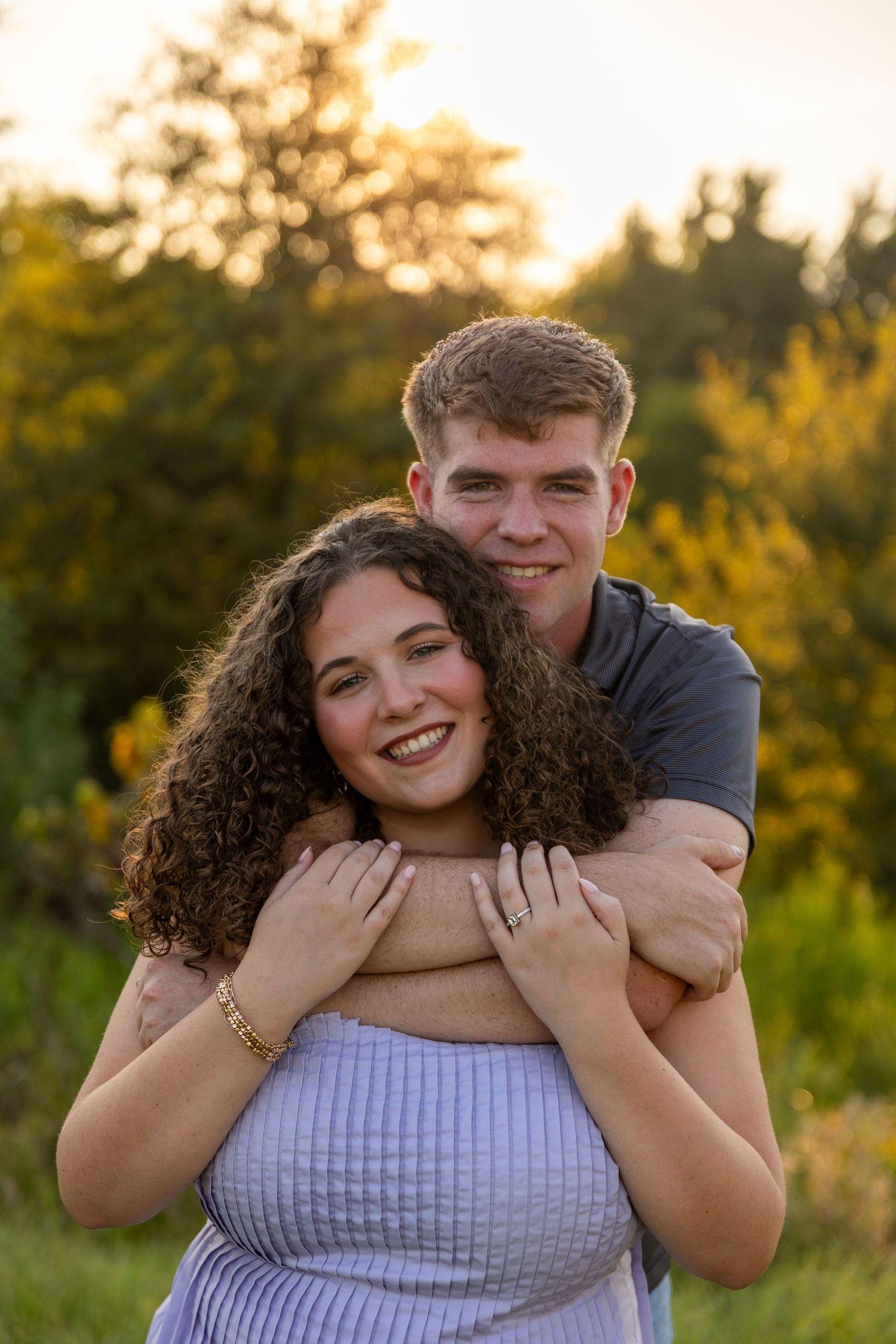 A joyful embrace between a couple during golden hour in a grassy field.