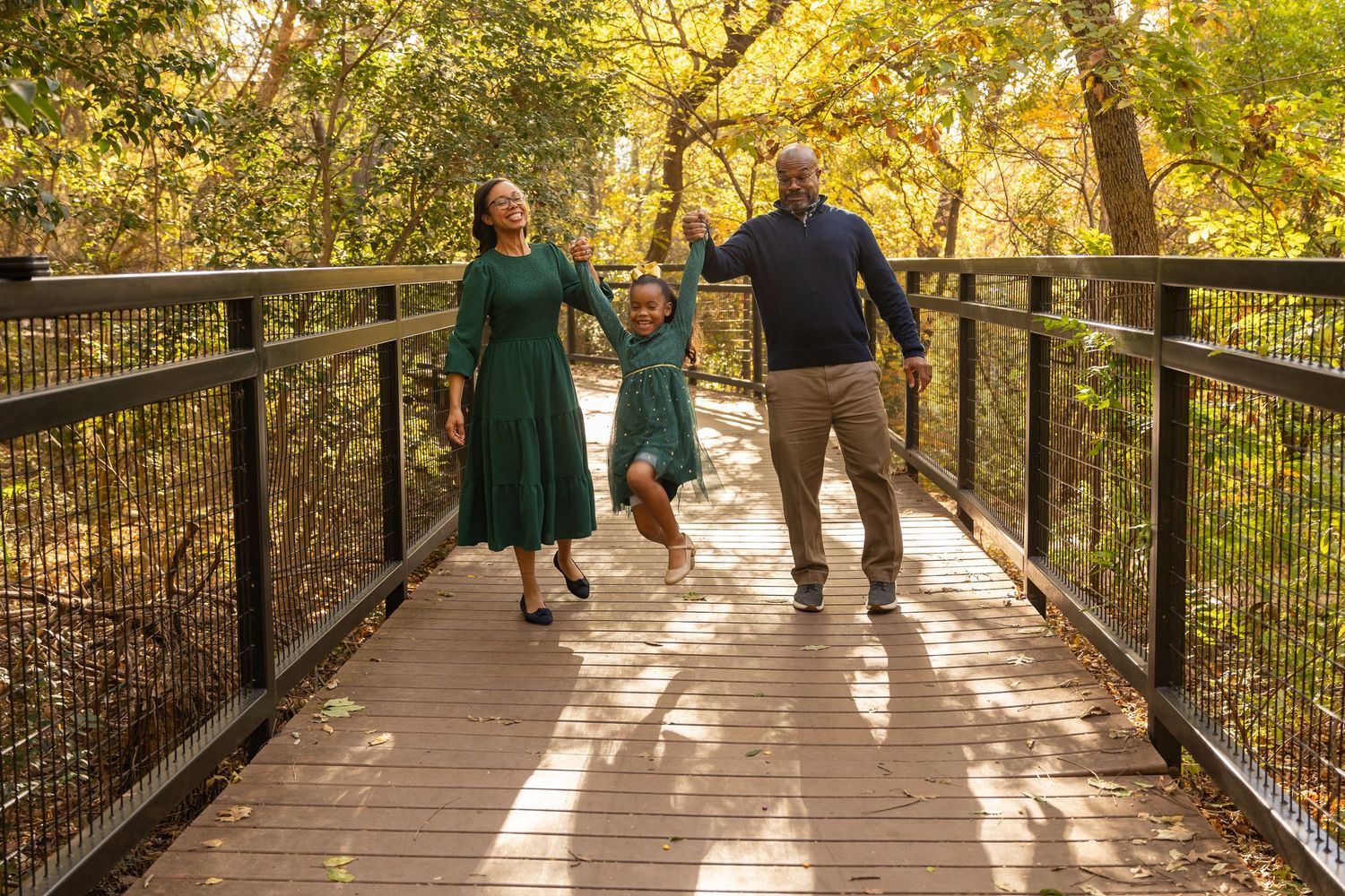 Family having fun on wooden bridge surrounded by fall foliage.