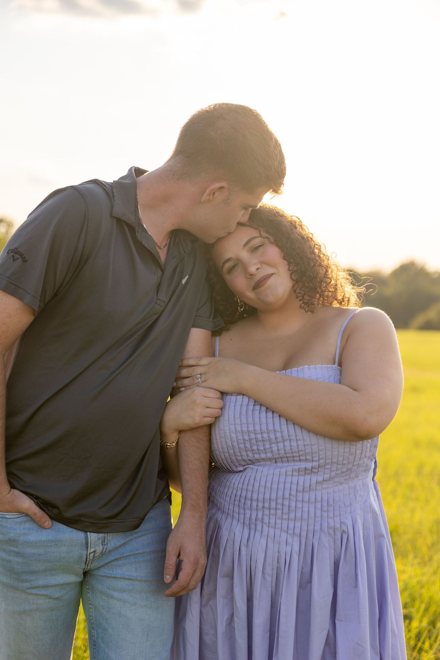 Couple embracing in a summer field with golden sunset light behind them.