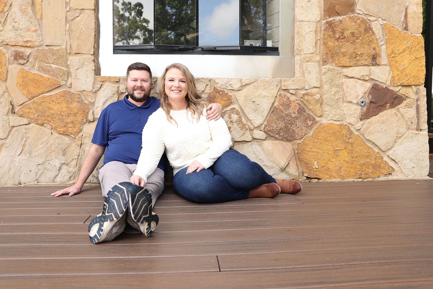 Couple relaxing on wooden deck against stone wall backdrop.