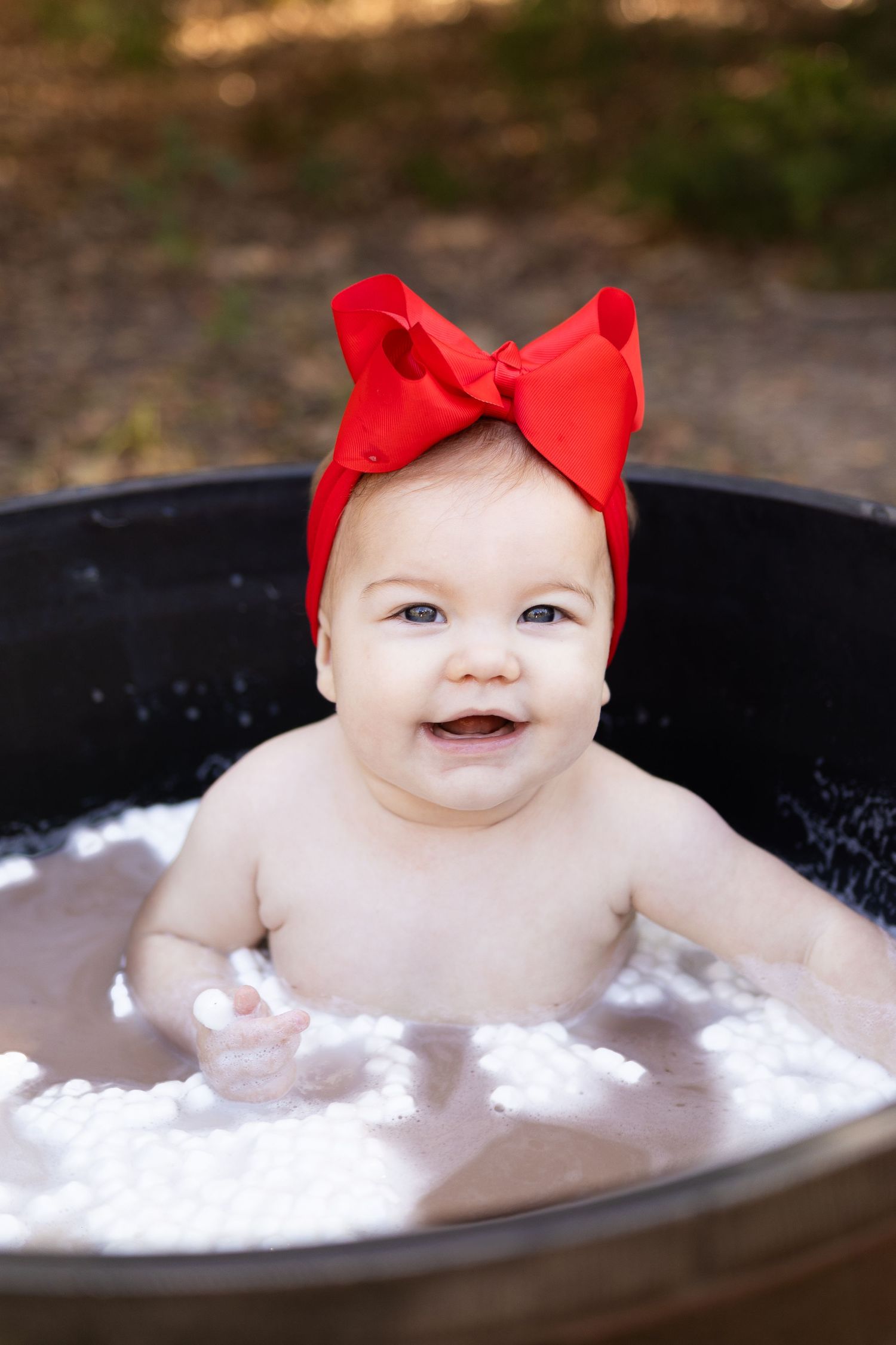 Baby in milk bath with red bow enjoying a relaxing soak.