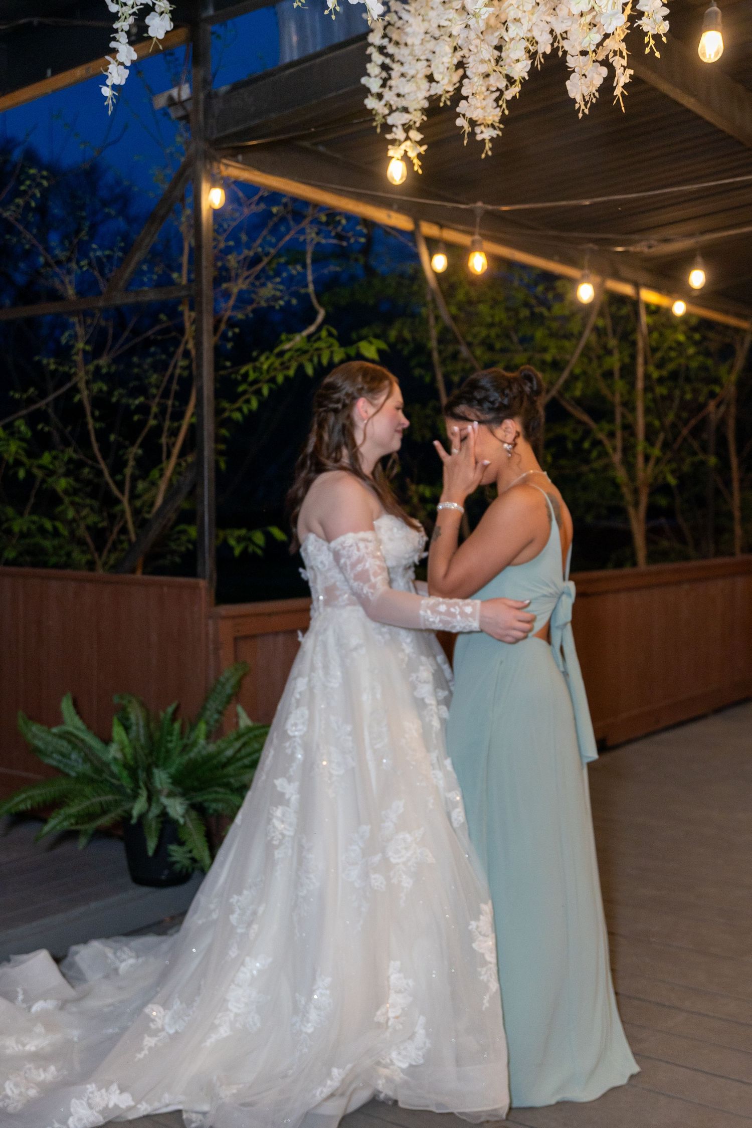 Evening wedding reception under string lights with couple in white dress and mint green attire.