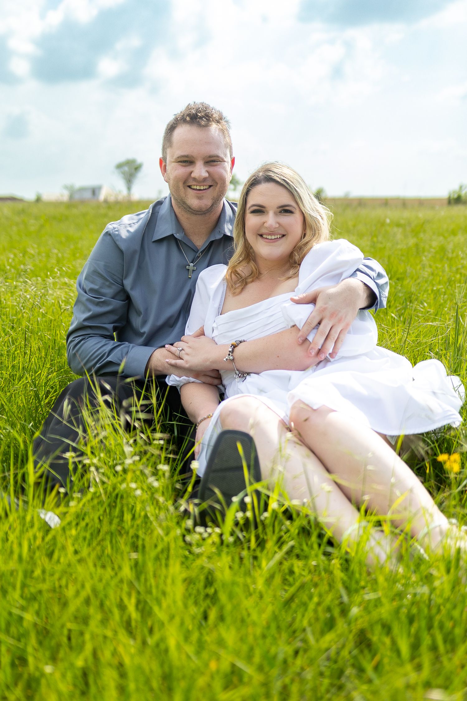 A couple relaxes together in a lush green field with wildflowers.