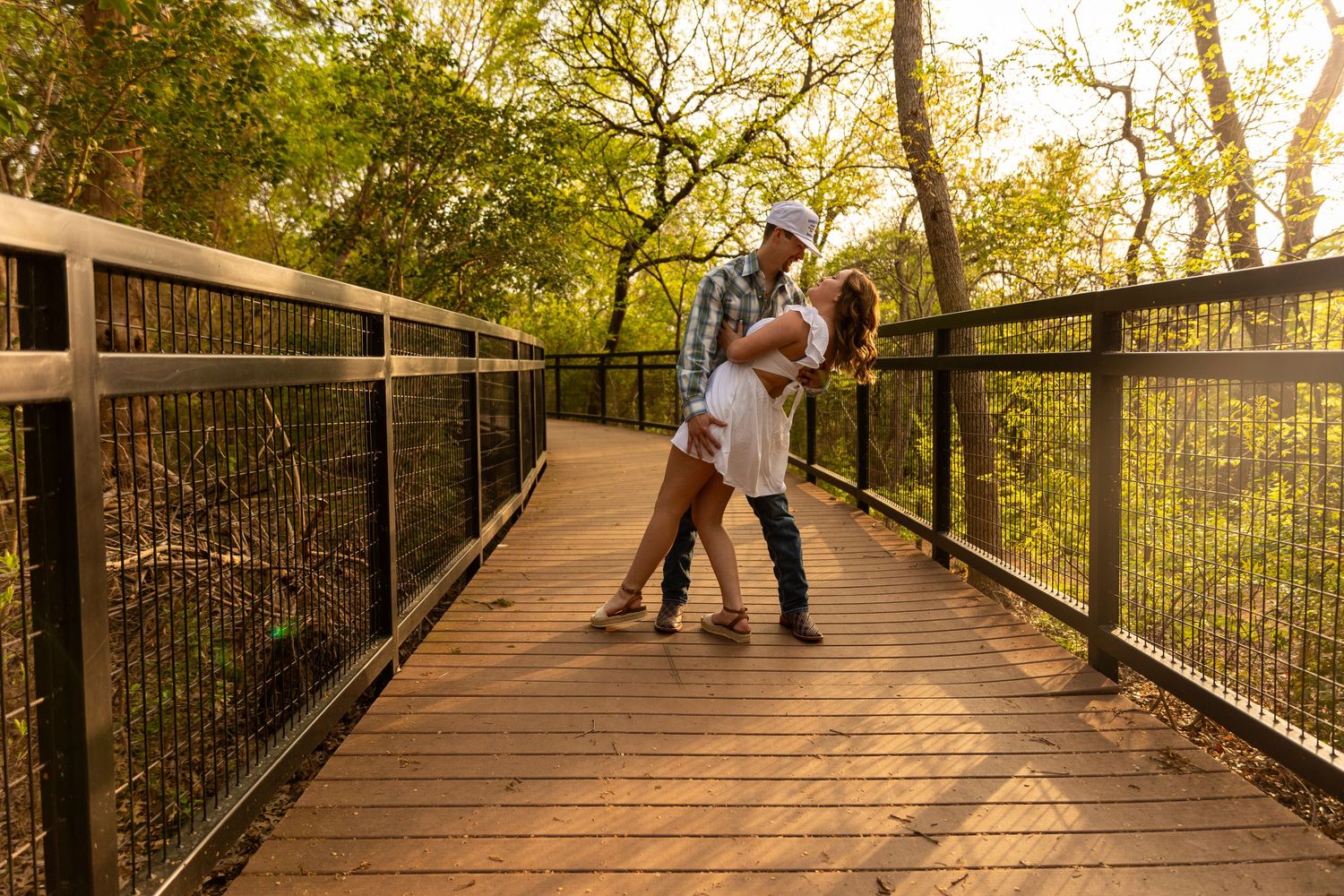 A romantic moment between a couple on a wooden bridge during sunset.