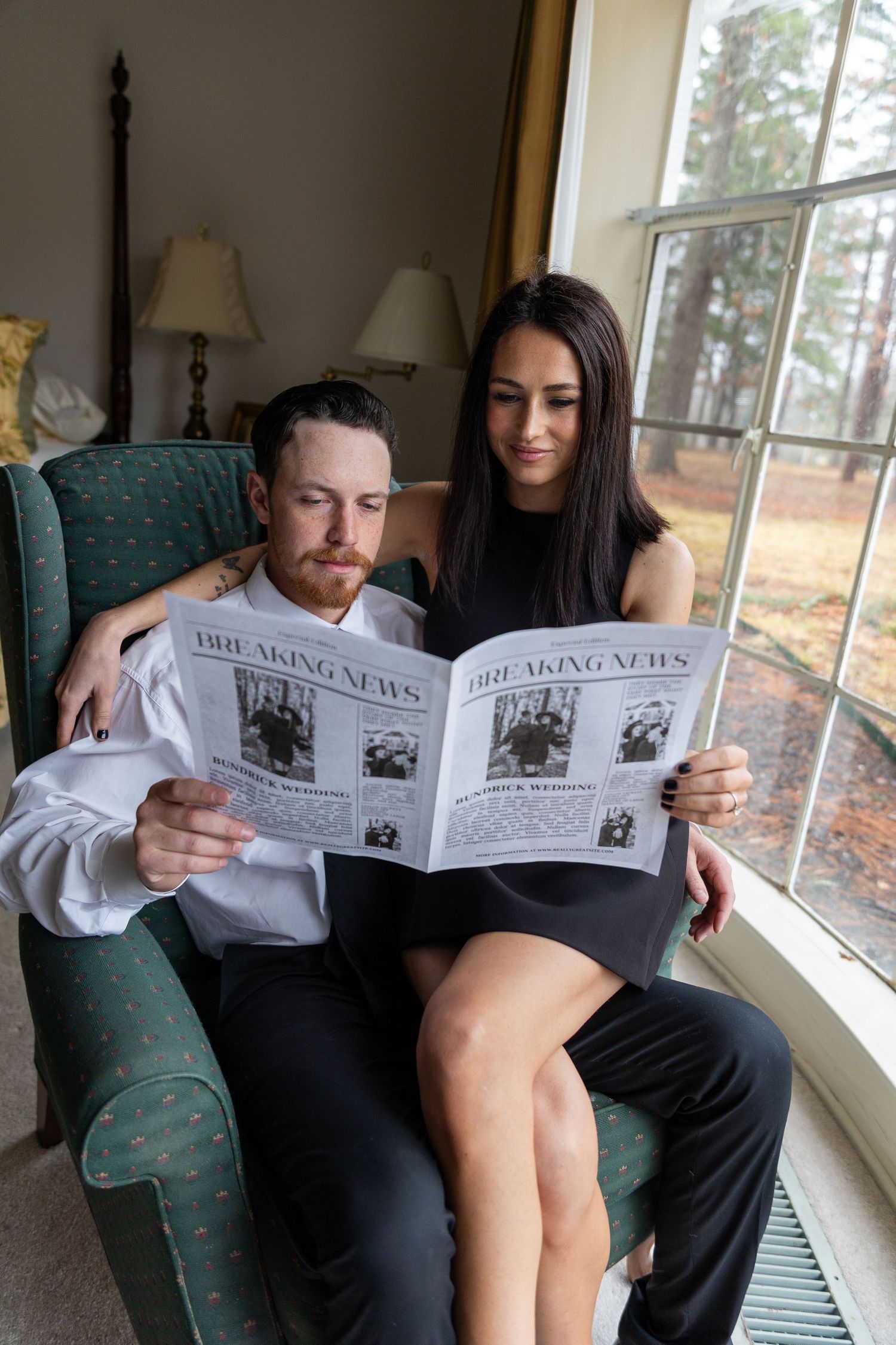 A couple relaxing in an armchair by a window while reading a newspaper together.