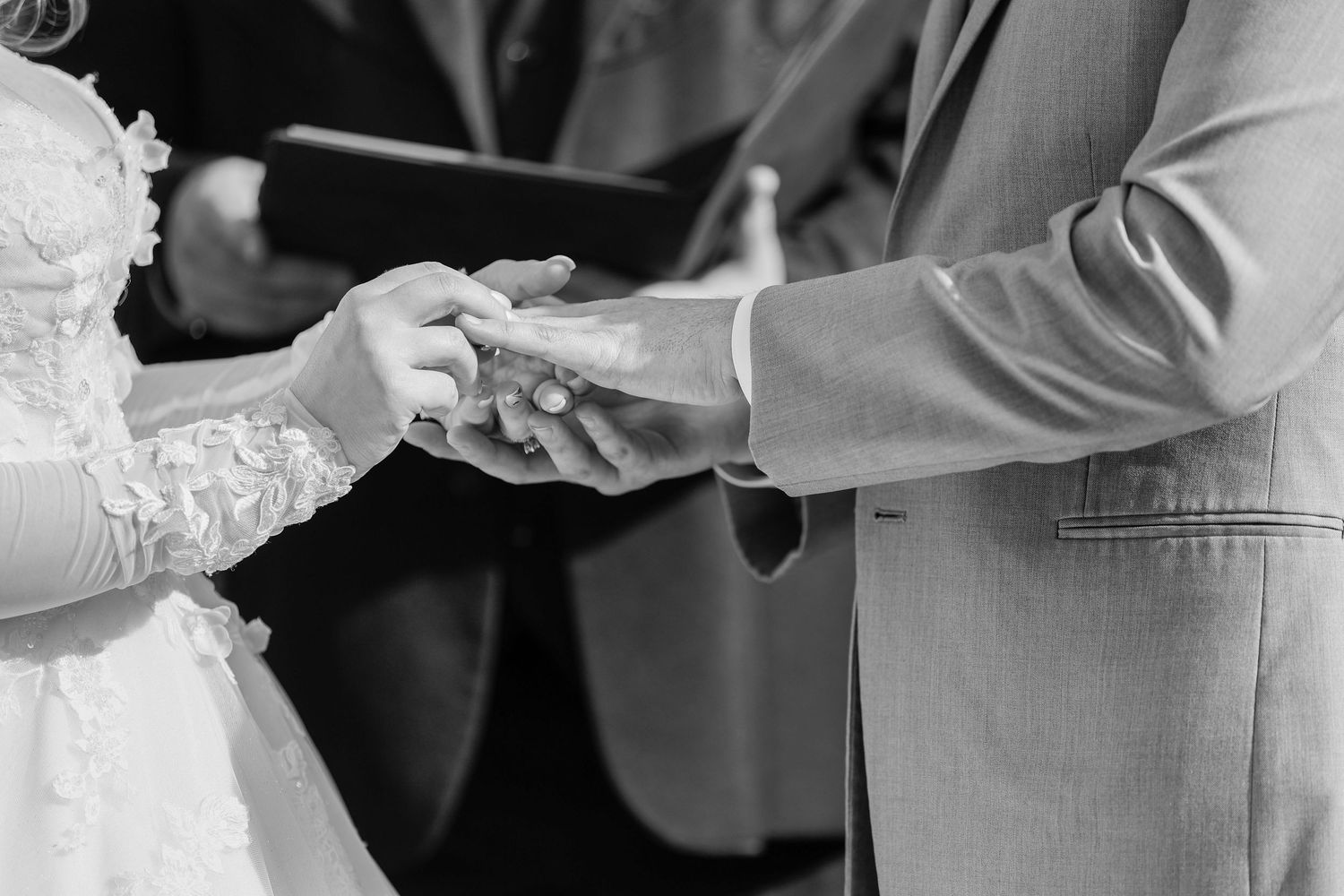 A black and white close-up of a couple exchanging rings during their wedding ceremony.