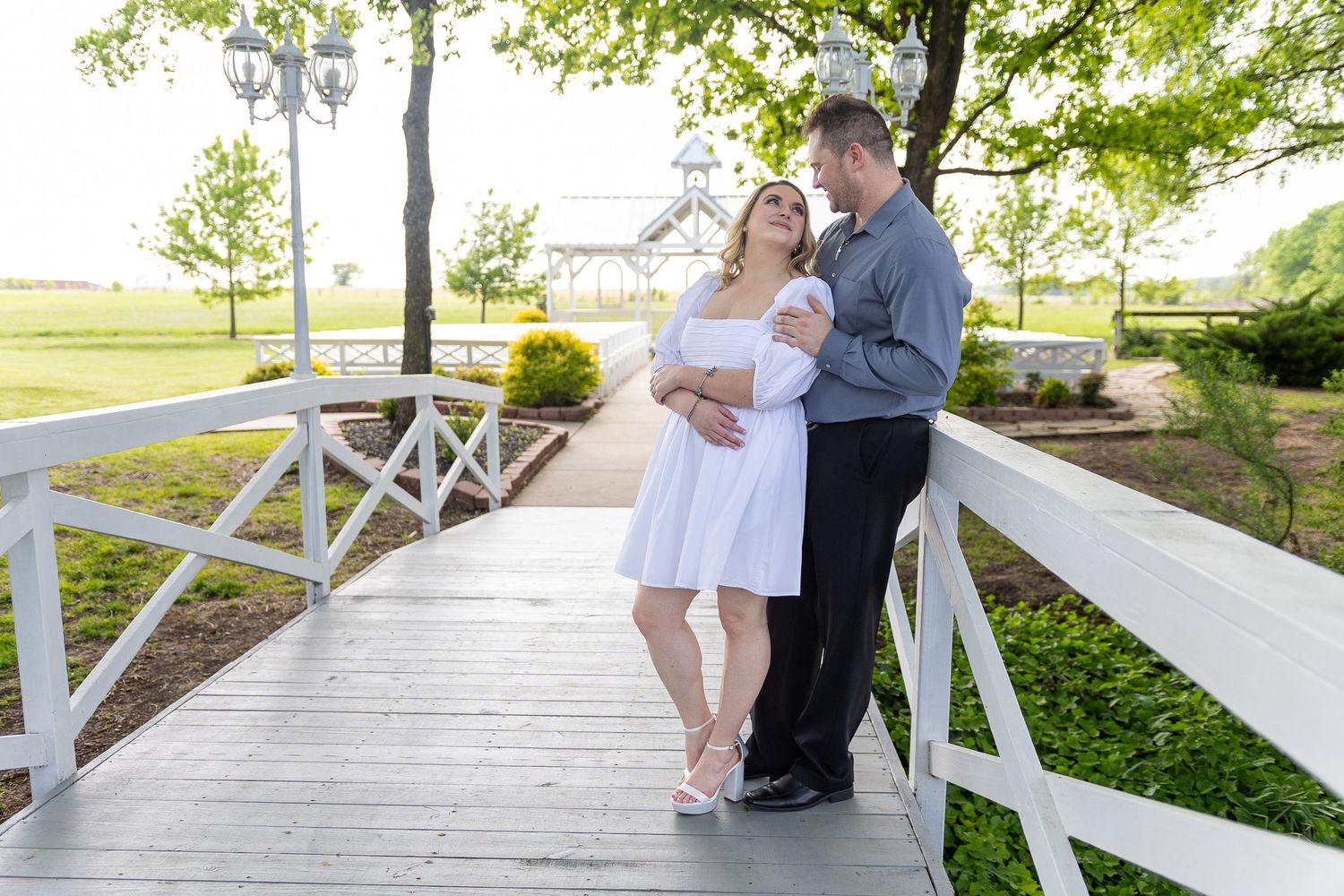 A couple poses together on a white bridge in a scenic outdoor setting.