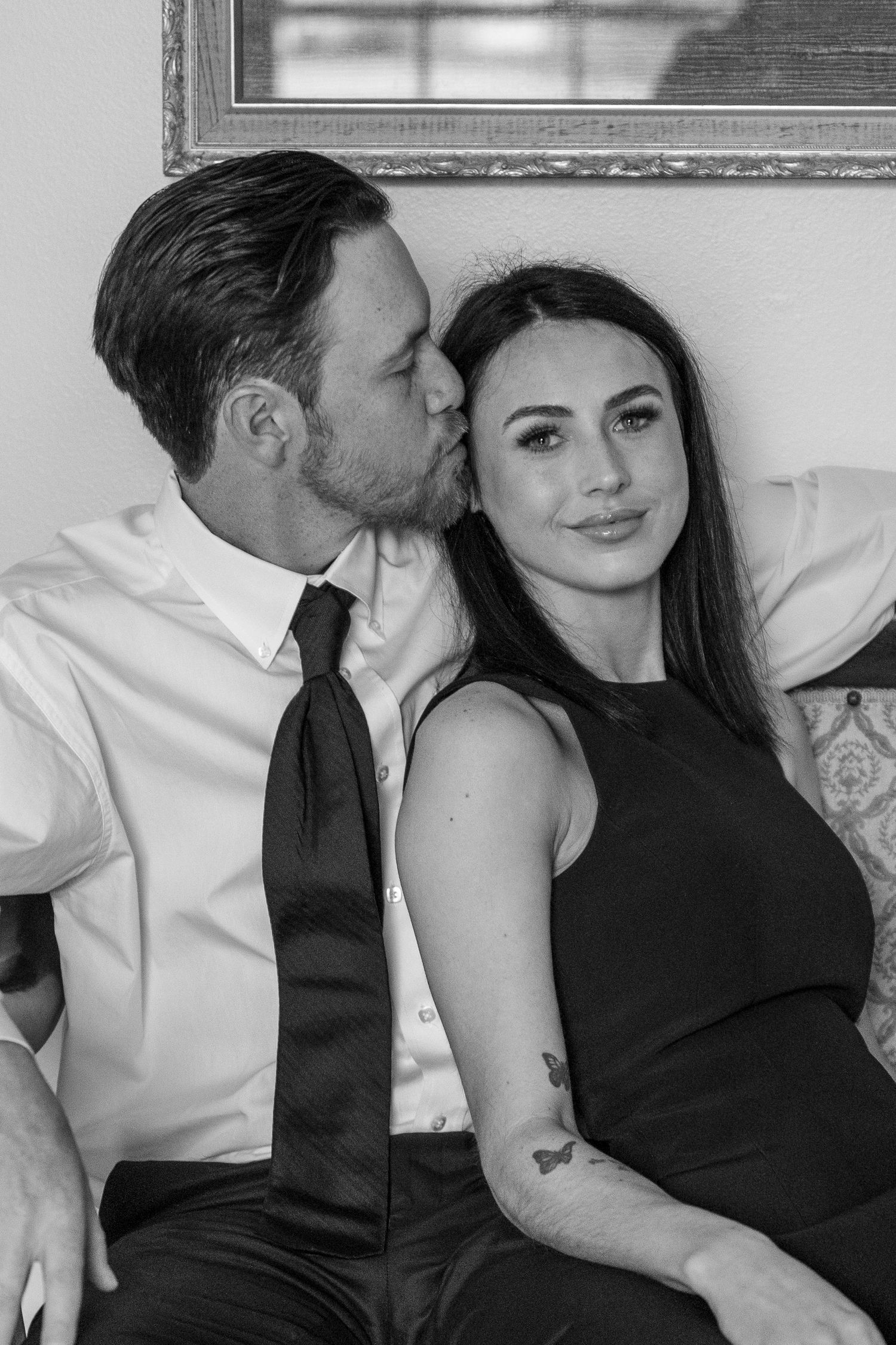An intimate black and white portrait of a couple in formal wear sharing a tender moment.