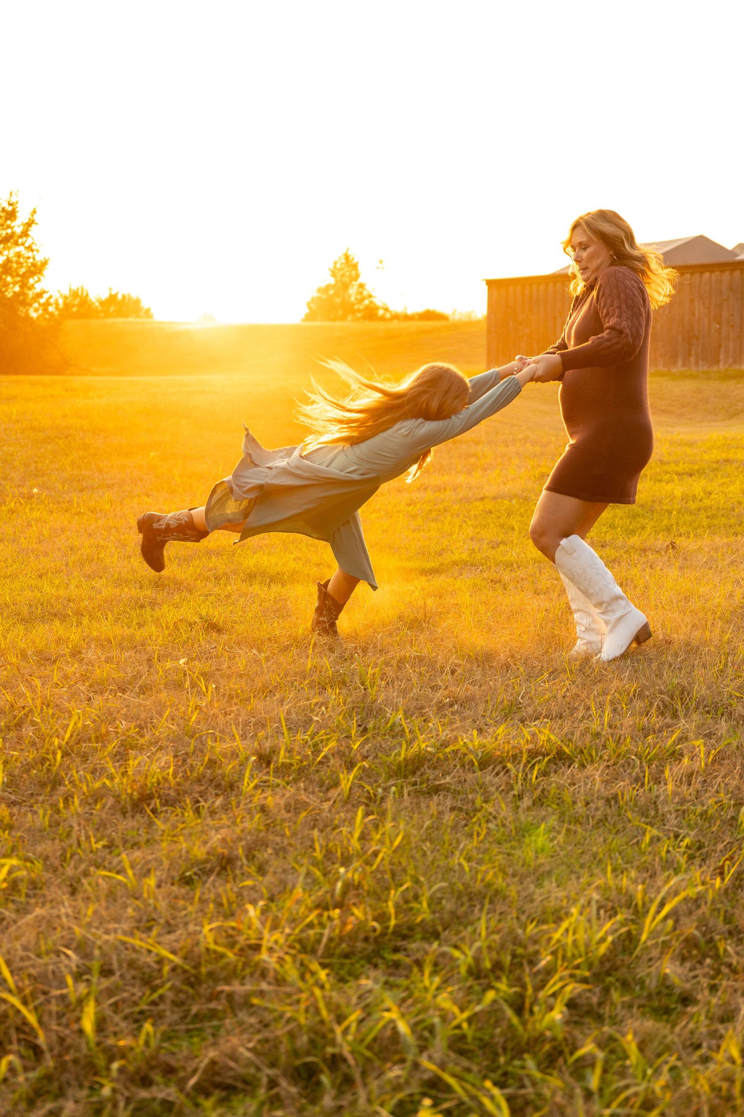 Two people playing and spinning in a golden sunlit field at sunset.
