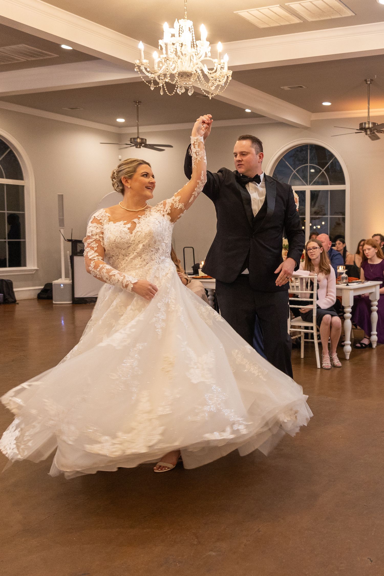 Wedding couple dancing in elegant ballroom under crystal chandeliers.