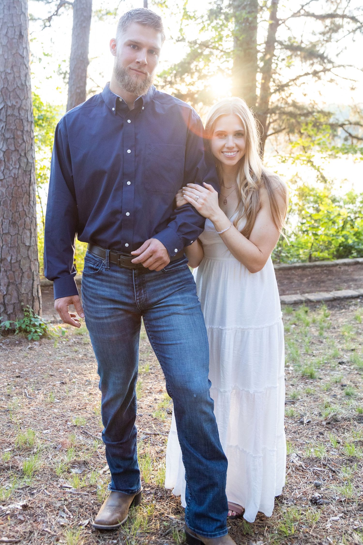 Couple walks together through sunlit forest setting during outdoor photoshoot.