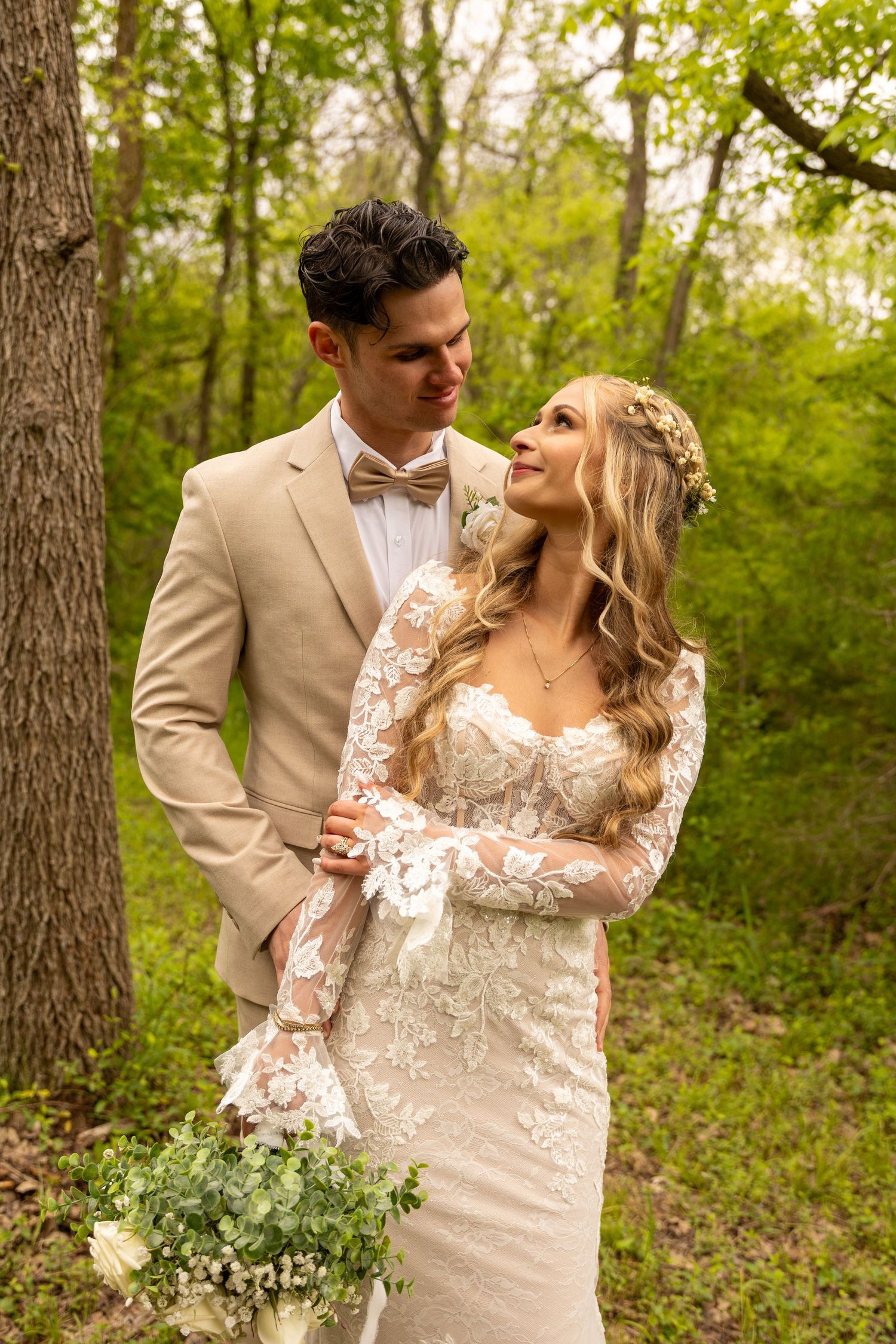 A romantic wedding portrait of a couple in a wooded setting with the bride holding a small bouquet.