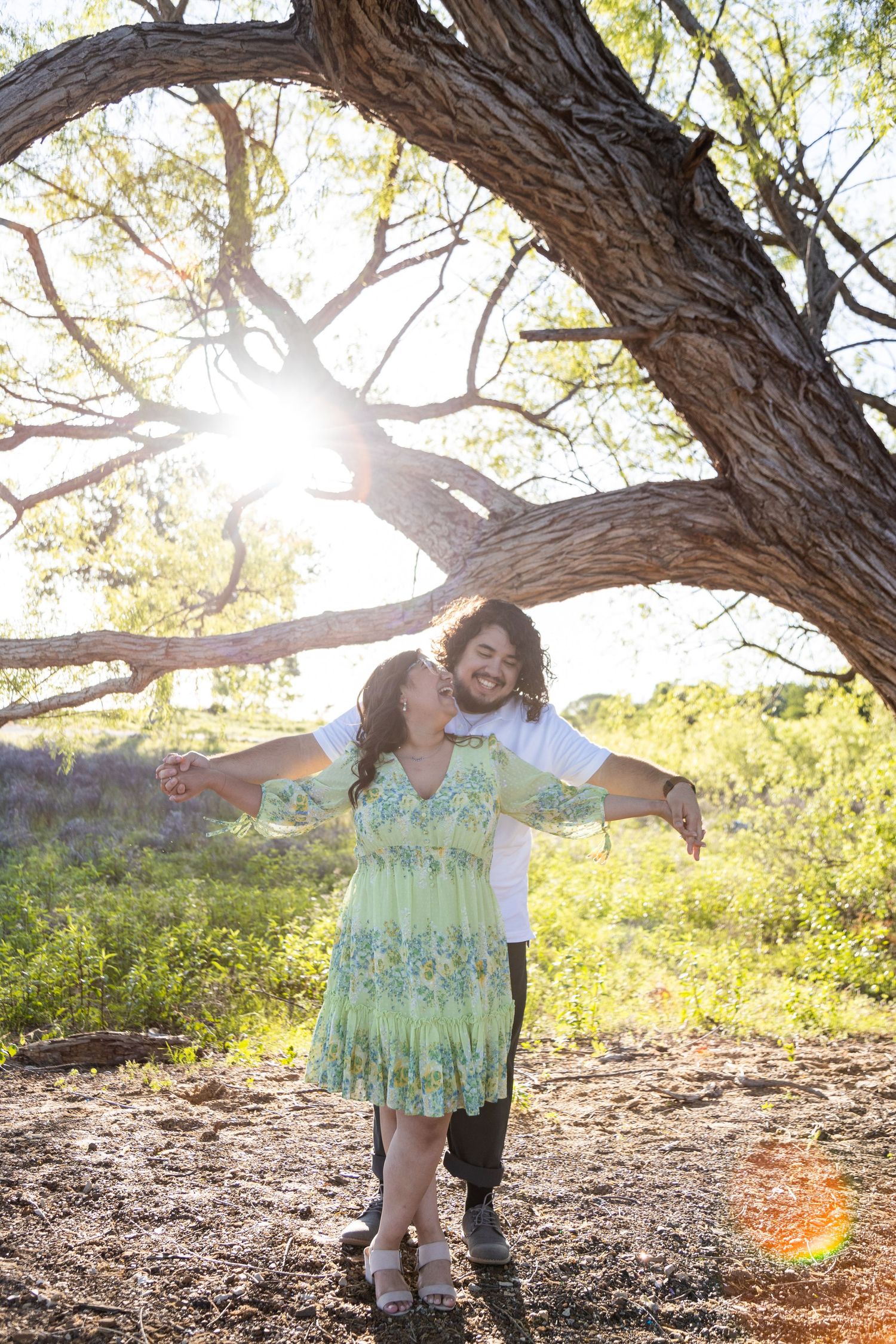 Romantic couple poses under tree branches during sunset photoshoot in nature.