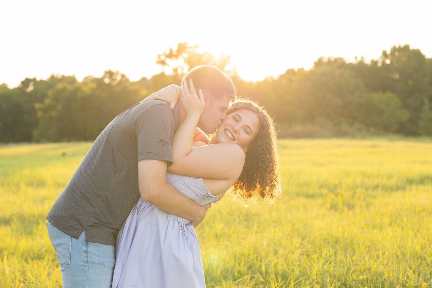A playful couple embraces in a sun-drenched field during golden hour.